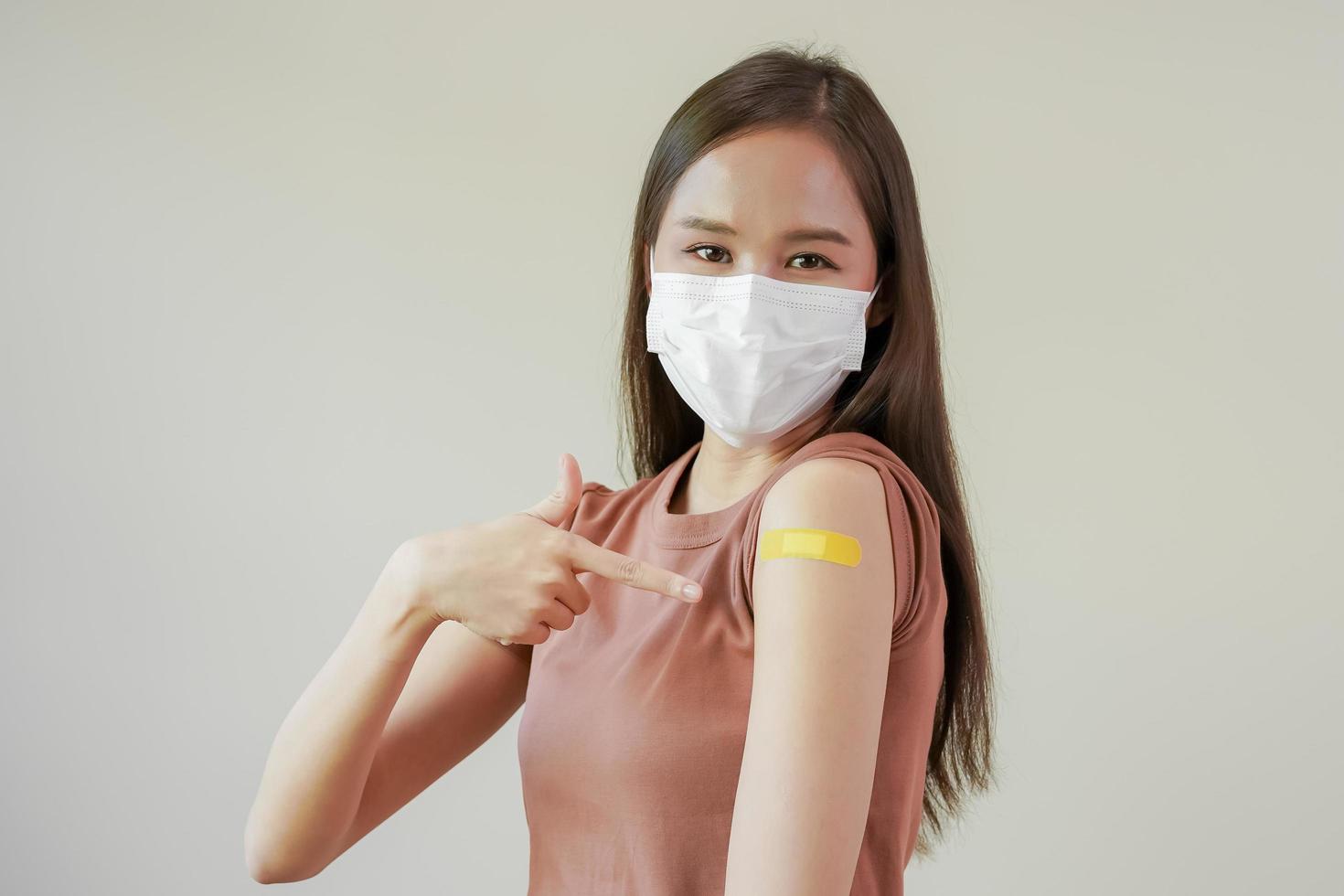 retrato de salud cuidado asiático joven mujer vistiendo cara máscara proteger, consiguiendo vacuna de COVID-19, influenza en casual, demostración brazo en amarillo vendaje, yeso, aislado en naturaleza fondo, Copiar espacio foto