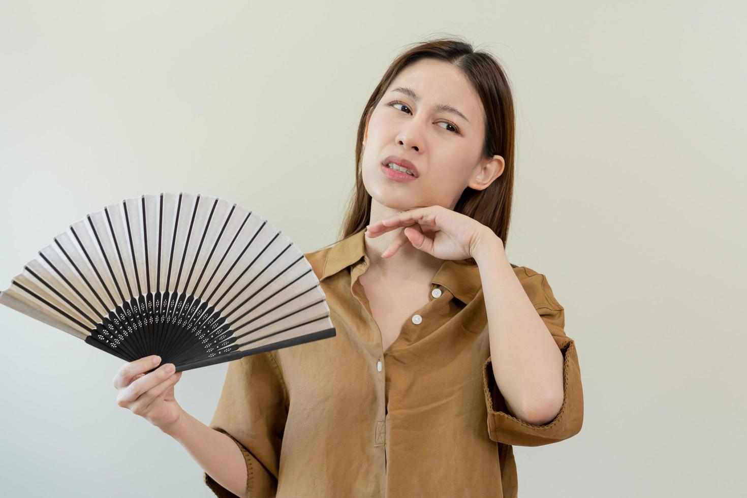 sufrimiento verano calor ataque, caliente clima, cansado asiático joven mujer, niña sudoroso y sediento, refrescante con mano en soplo, ola ventilador a ventilación cuando temperatura alto a hogar, casa.en antecedentes foto