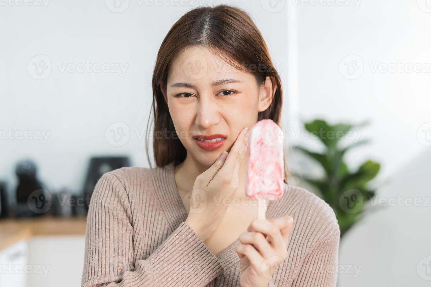 salud asiático joven mujer conmovedor mejilla, expresión, sufrimiento desde dolor de muelas, decaer o sensibilidad cavidad molar diente, dientes o inflamación comer frío hielo crema a hogar. sensible dientes gente. foto