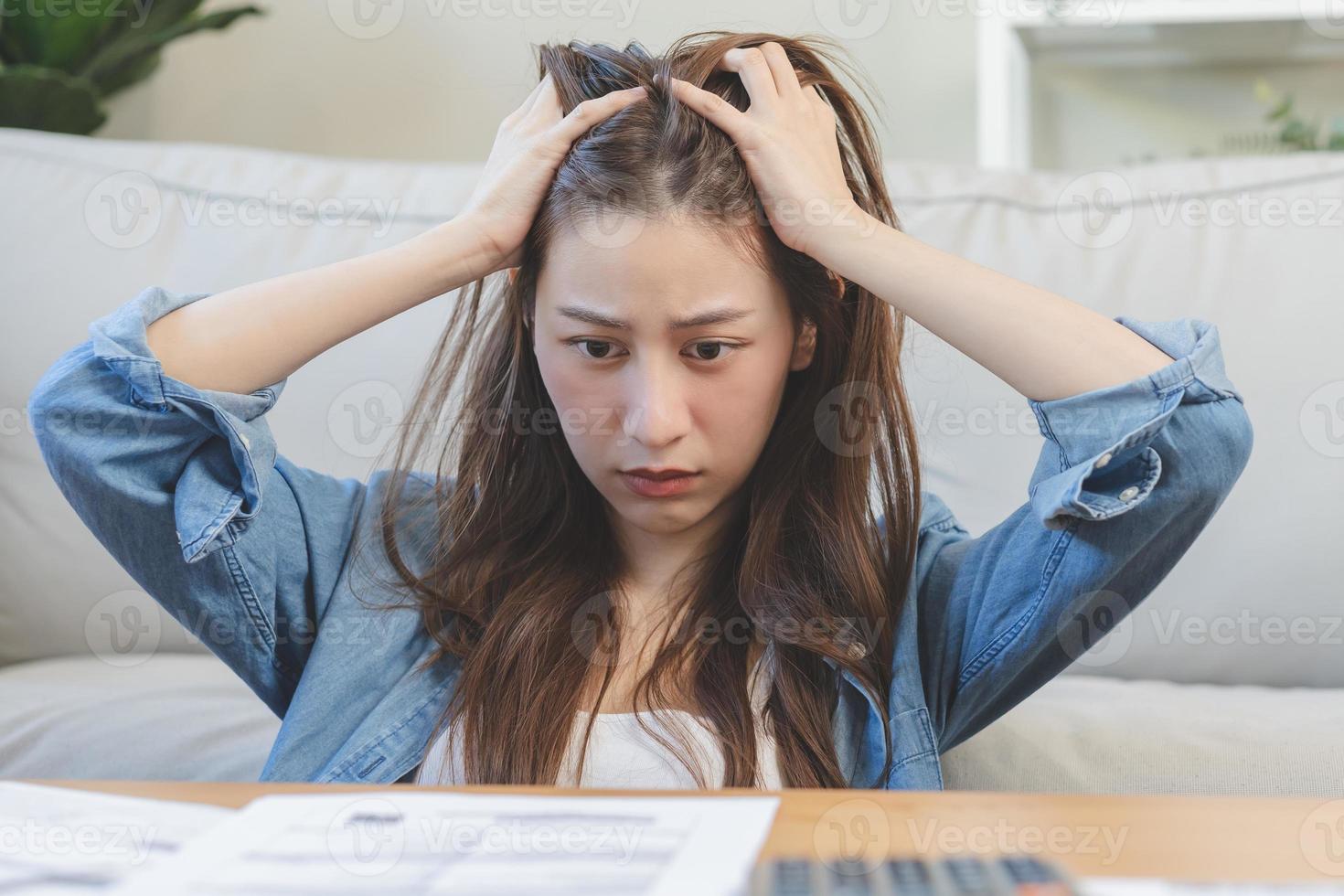 Financial owe asian woman, female hand in cover face, sitting in stressed and confused by calculate expense from invoice or bill, have no money to pay, mortgage or loan. Debt, bankruptcy or bankrupt. photo
