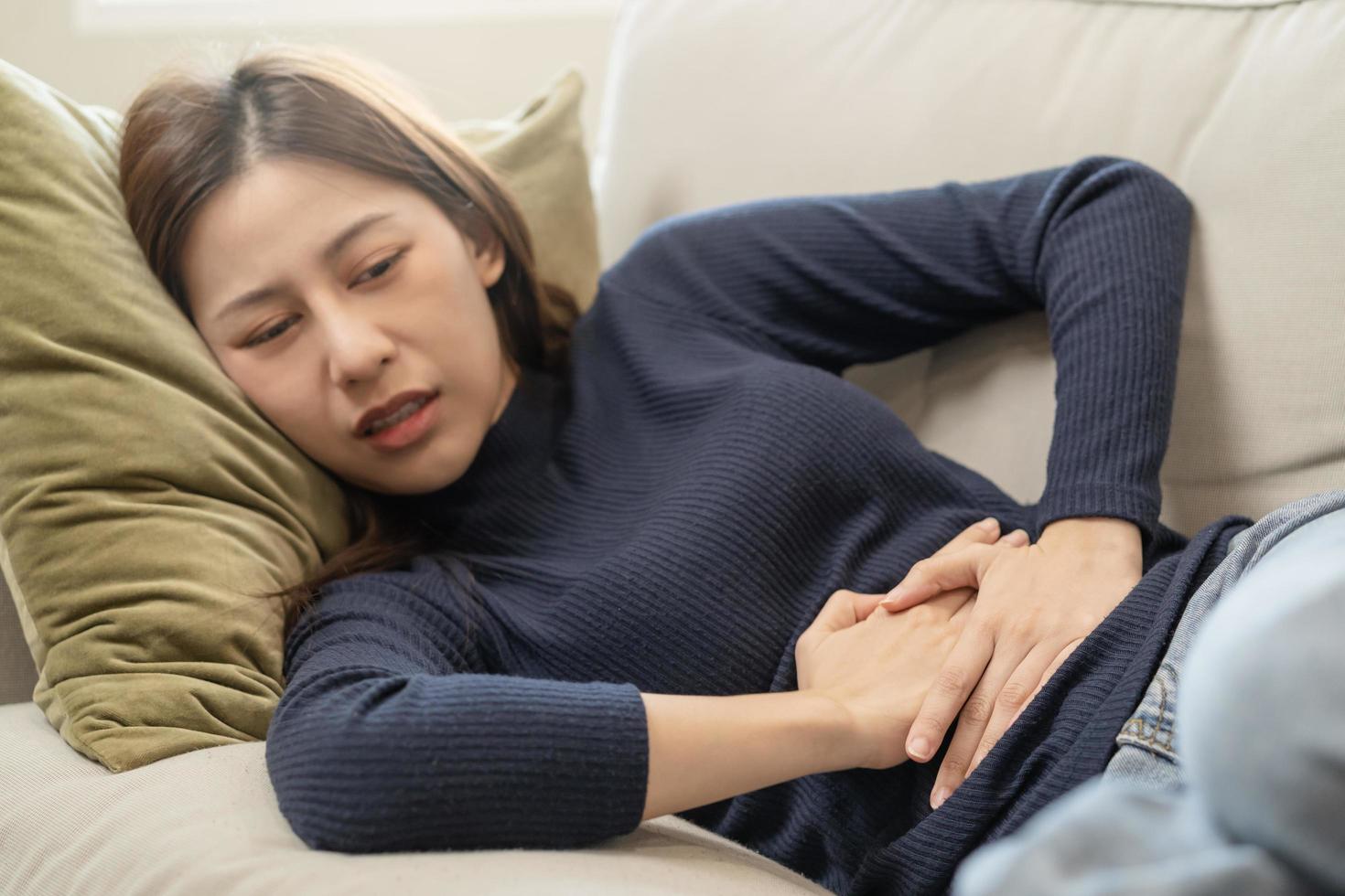 flatulencia asiático joven mujer, niña mano en estómago dolor, sufrir desde comida envenenamiento, abdominal dolor y colon problema, gastritis o diarrea. paciente barriga, abdomen o inflamación, concepto. foto