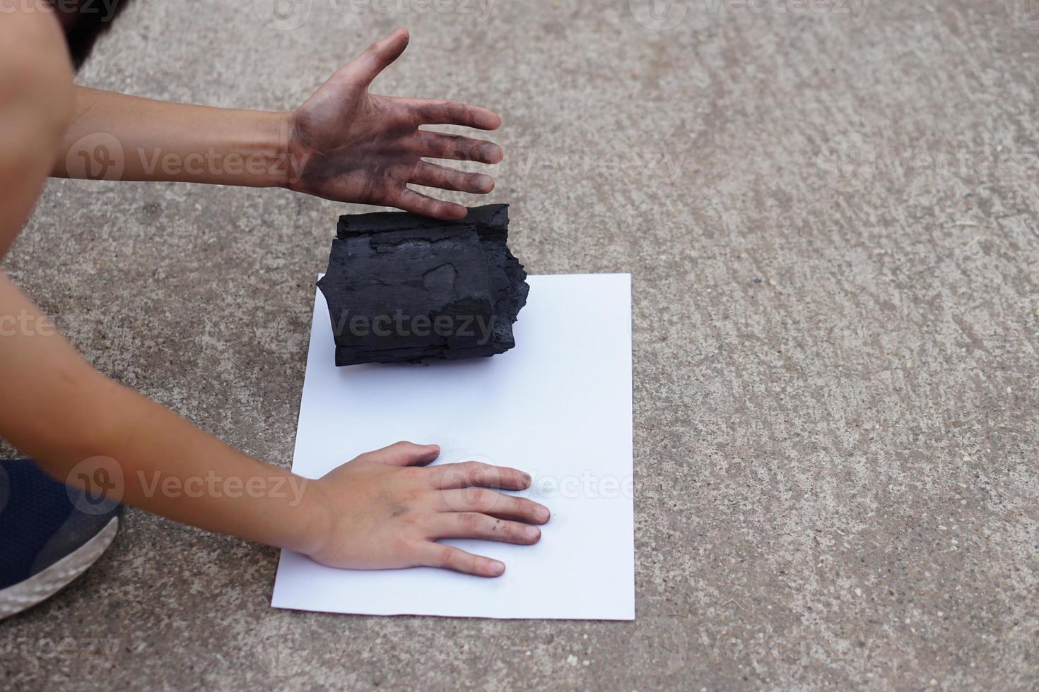 Closeup boy stamped his dirty hand with black stain of charcoal on white paper, make hand print graffiti. Concept, learning by doing. Touch and observe  in science subject activity. Nature fuel photo