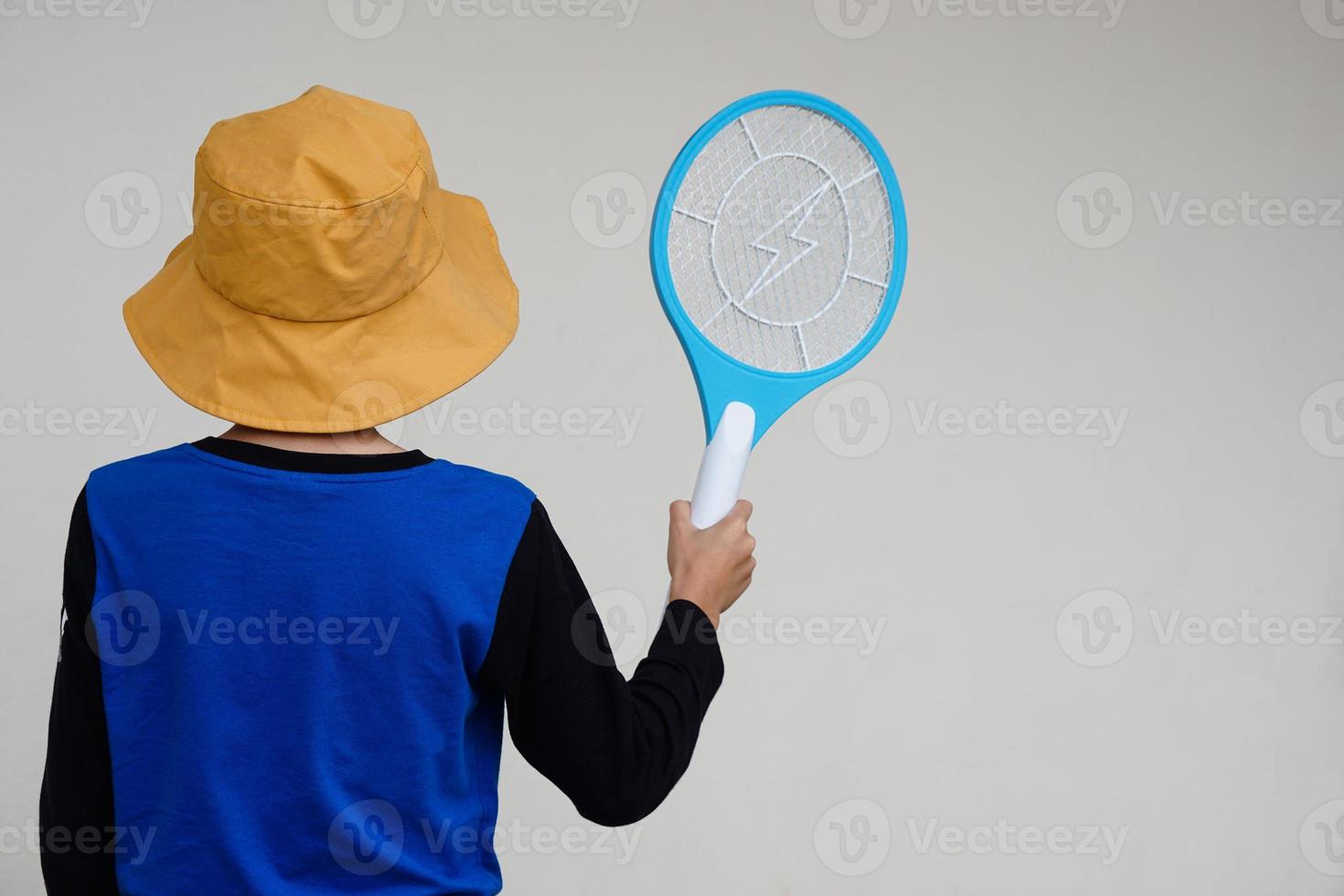 Back view of boy wears hat, blue shirt, holds mosquito electric swatter racket. Concept, electric device to kill mosquitoes, insects, bugs by swatting to flying insects photo