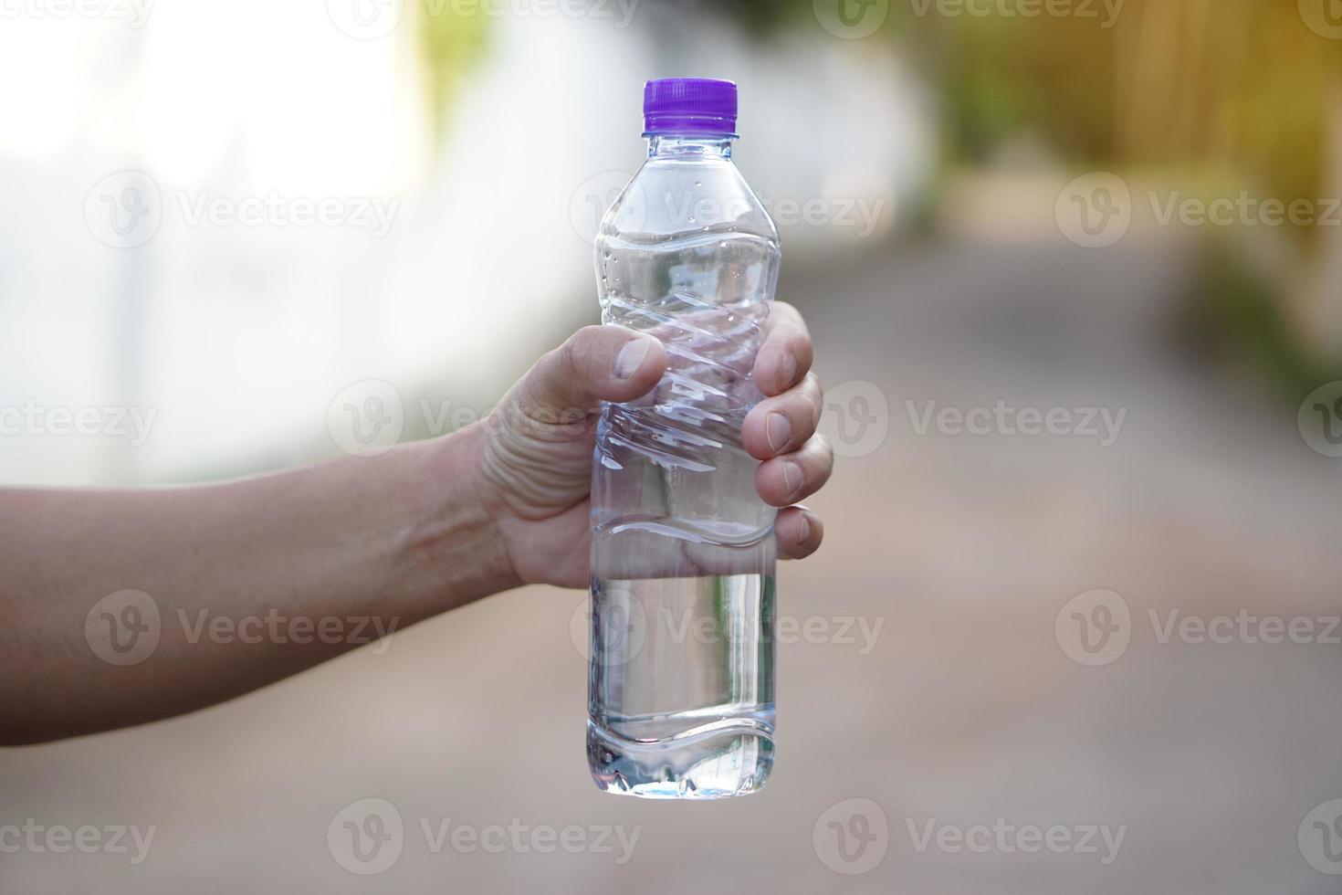 Closeup hand holds drinking water bottle with purple cap. Concept , Drinking water for health, Healthy lifestyle. Quenching thirst, reduce fatigue, refresh body. photo