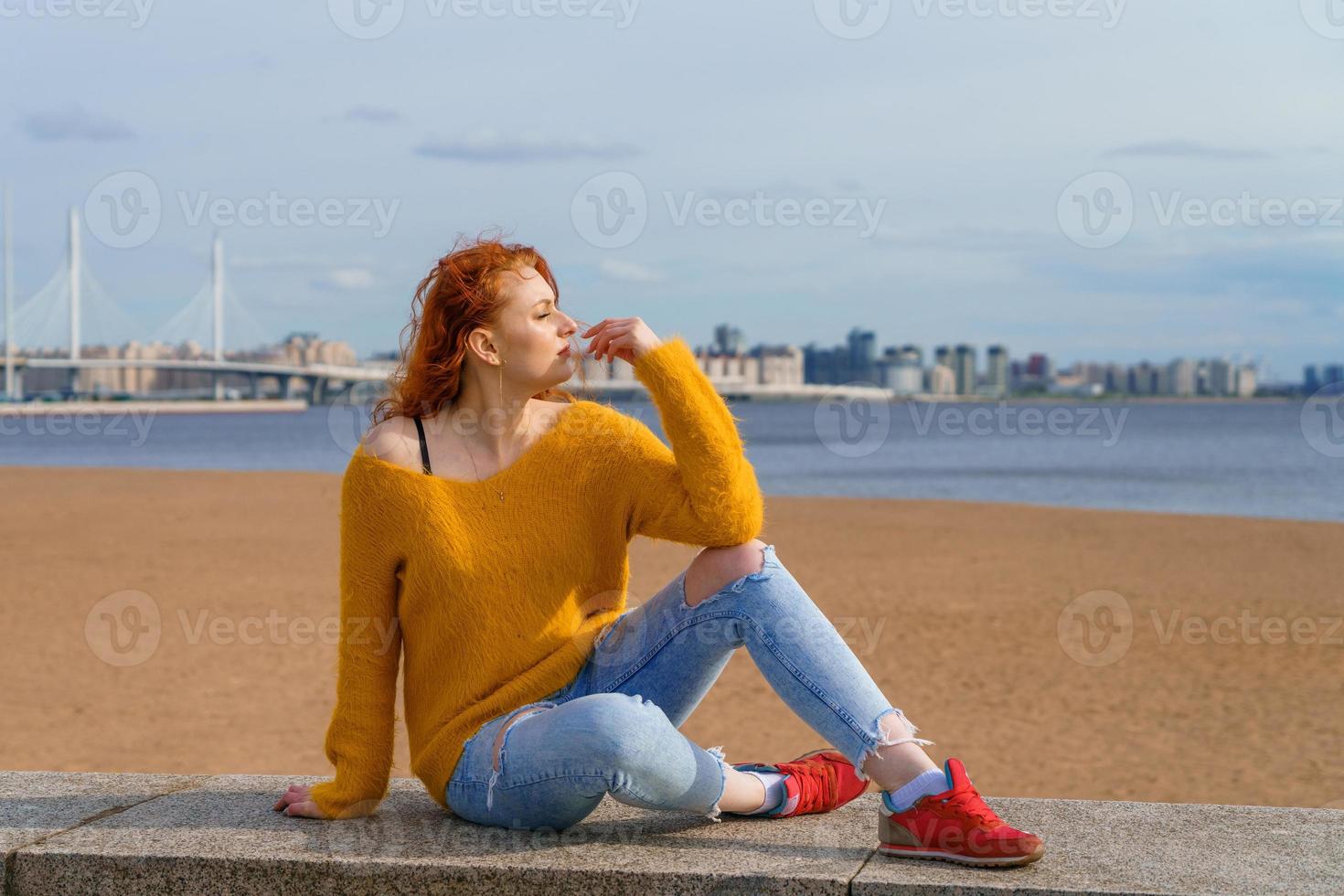 atractivo joven pelirrojo mujer sentado fuera de en frente al mar, vistiendo amarillo foto