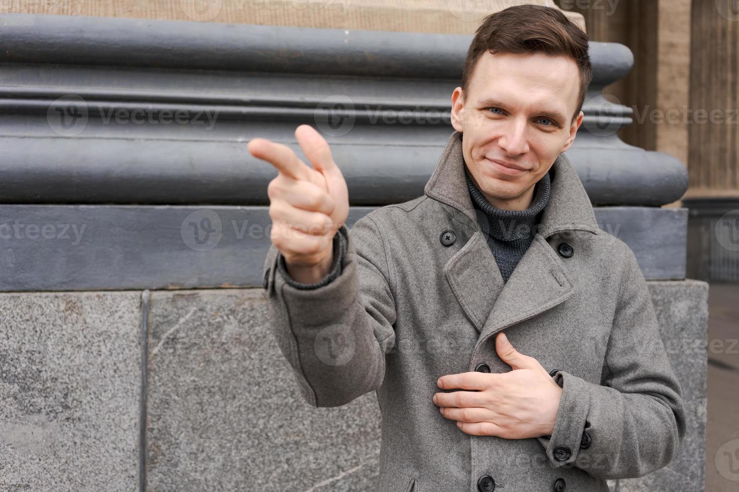 Young man in dark clothes on street. Caucasian guy in gray coat, smiles photo