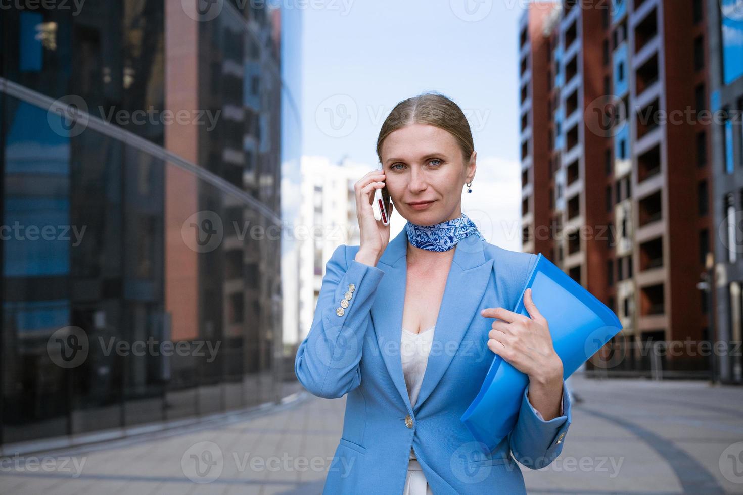 negocio mujer en azul hablando en el teléfono con un carpeta en su mano foto