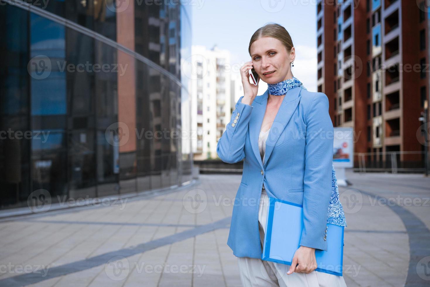 negocio mujer en azul hablando en el teléfono con un carpeta en su mano foto