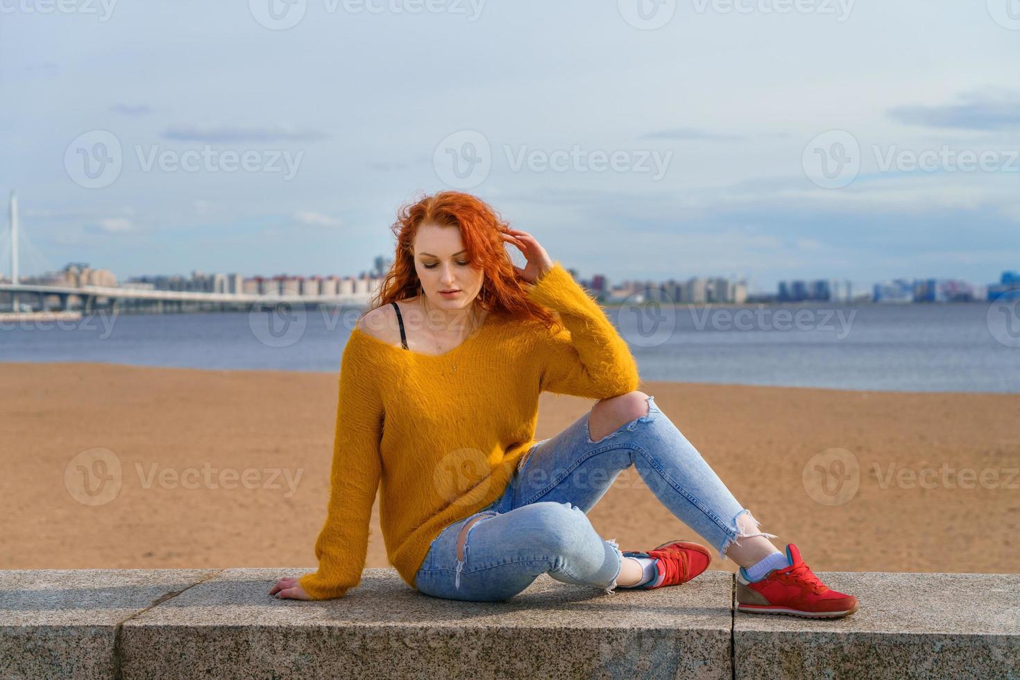 Young red-haired girl in yellow sweater and jeans. Pretty woman sits photo