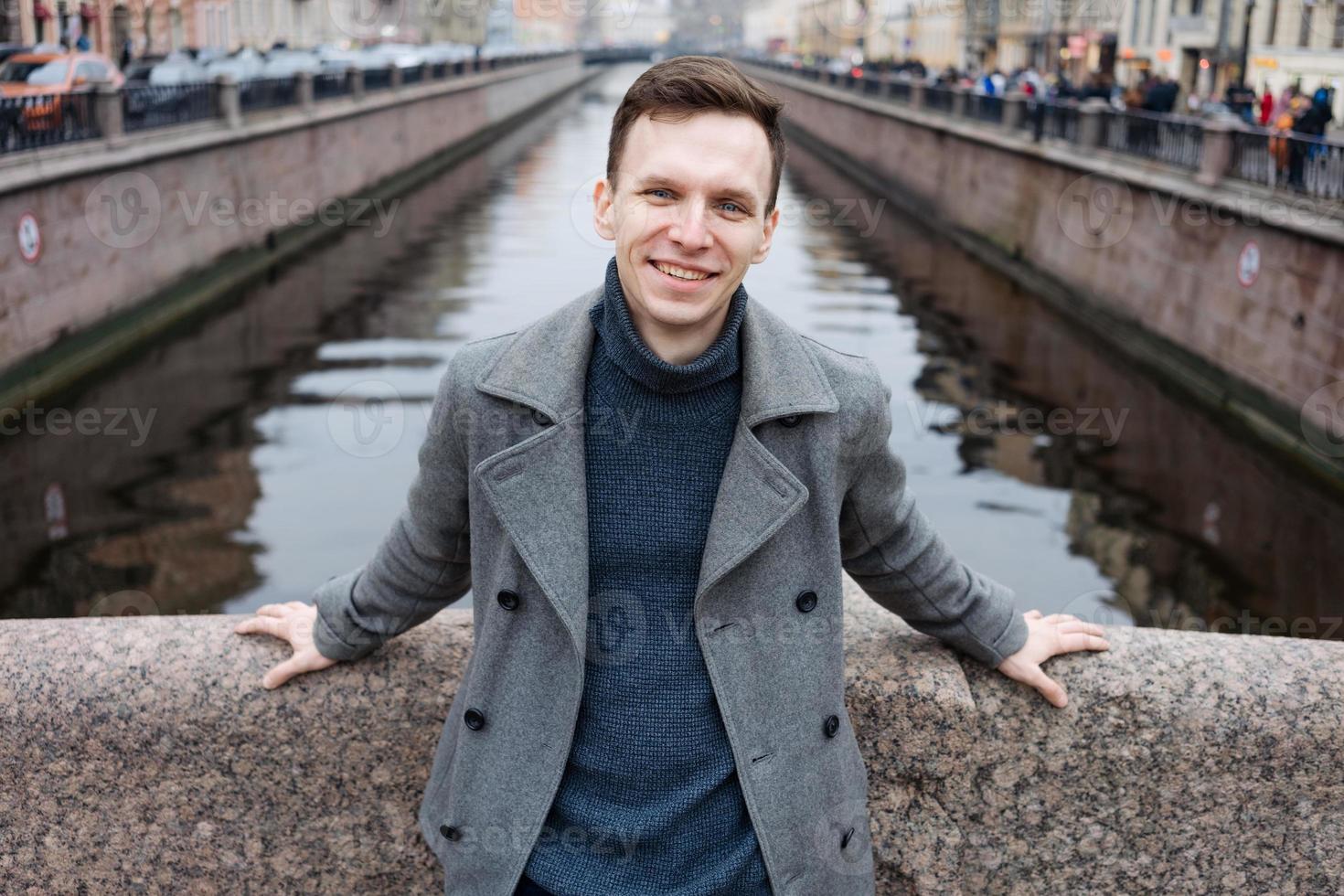 Man in winter scarf and gray coat is standing, leaning on pavement railing photo