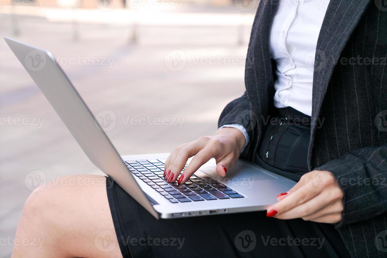 Young serious business woman with laptop studying online while sitting on bench photo