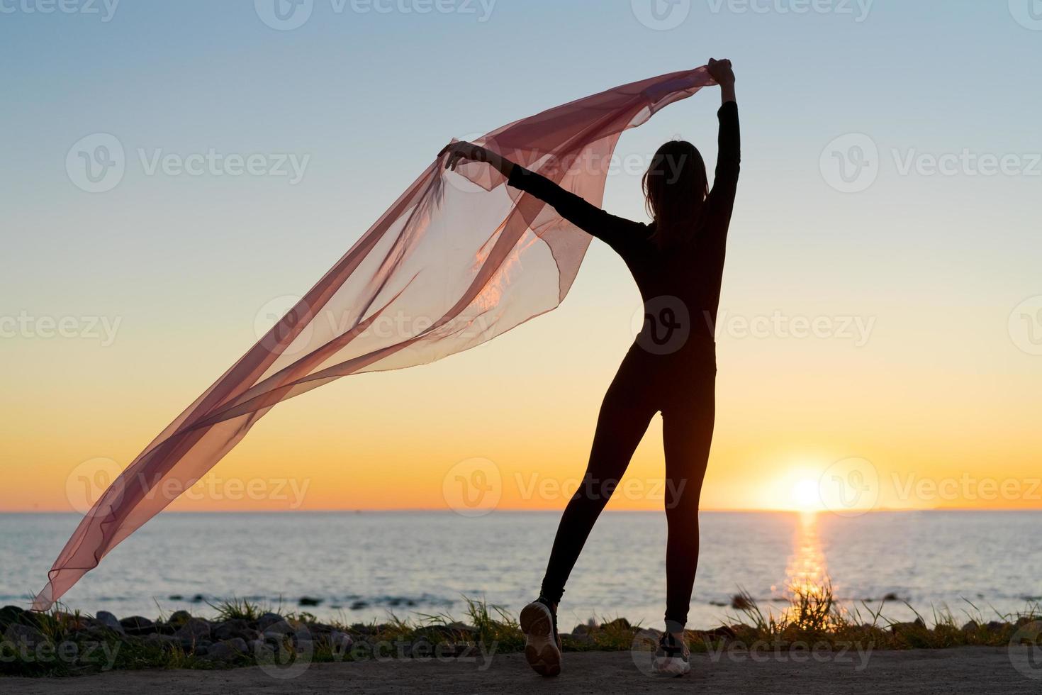 Silhouette slender girl at sunset on seashore rejoices with a transparent cloth photo