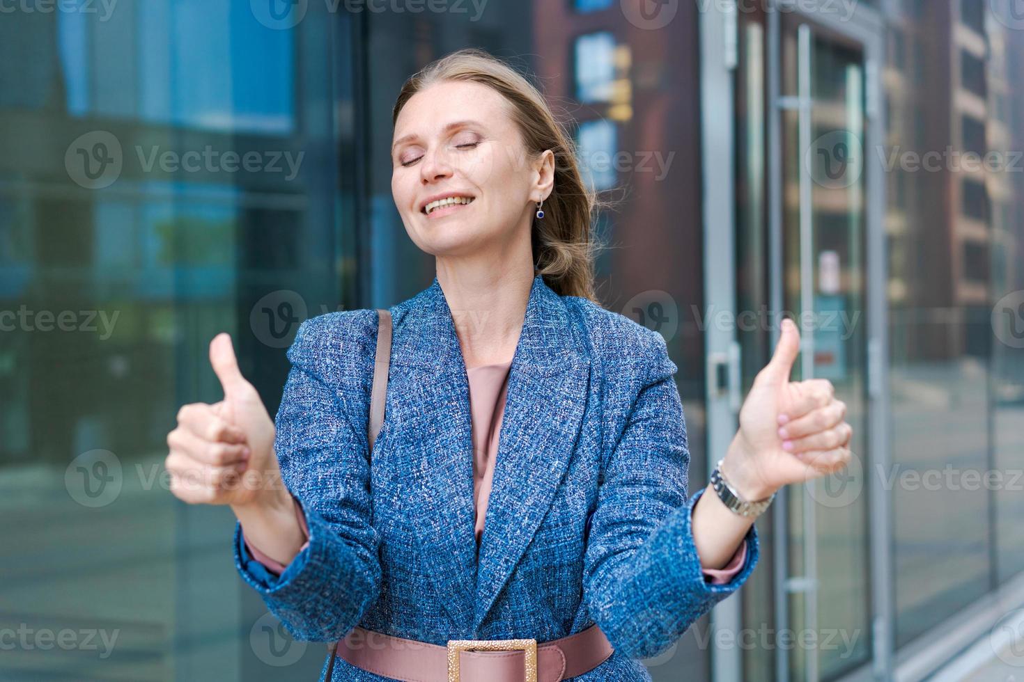 Happy business woman showing thumbs up while standing outdoors against office photo