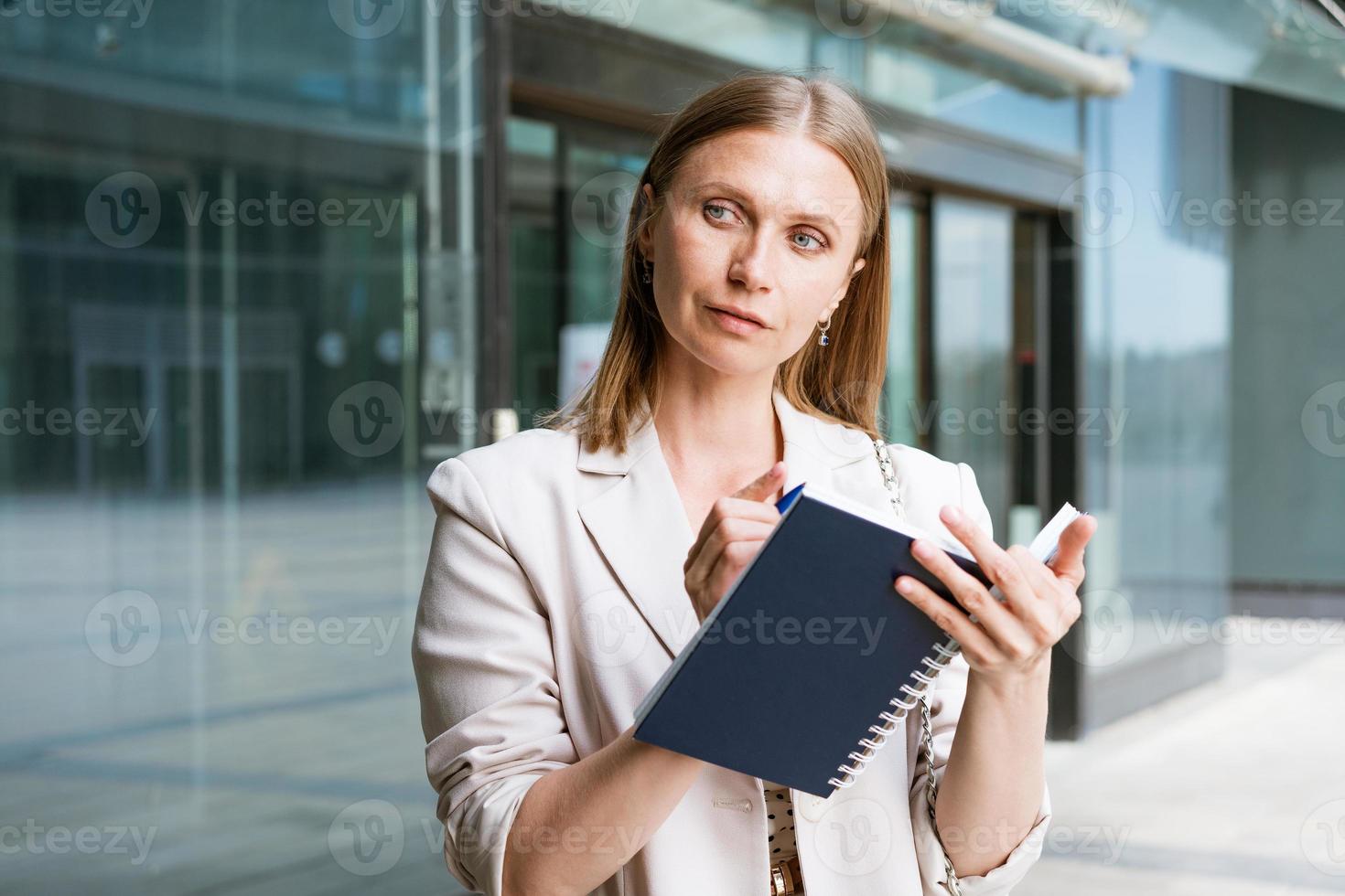 Business woman in light jacket stands and writes something near business photo