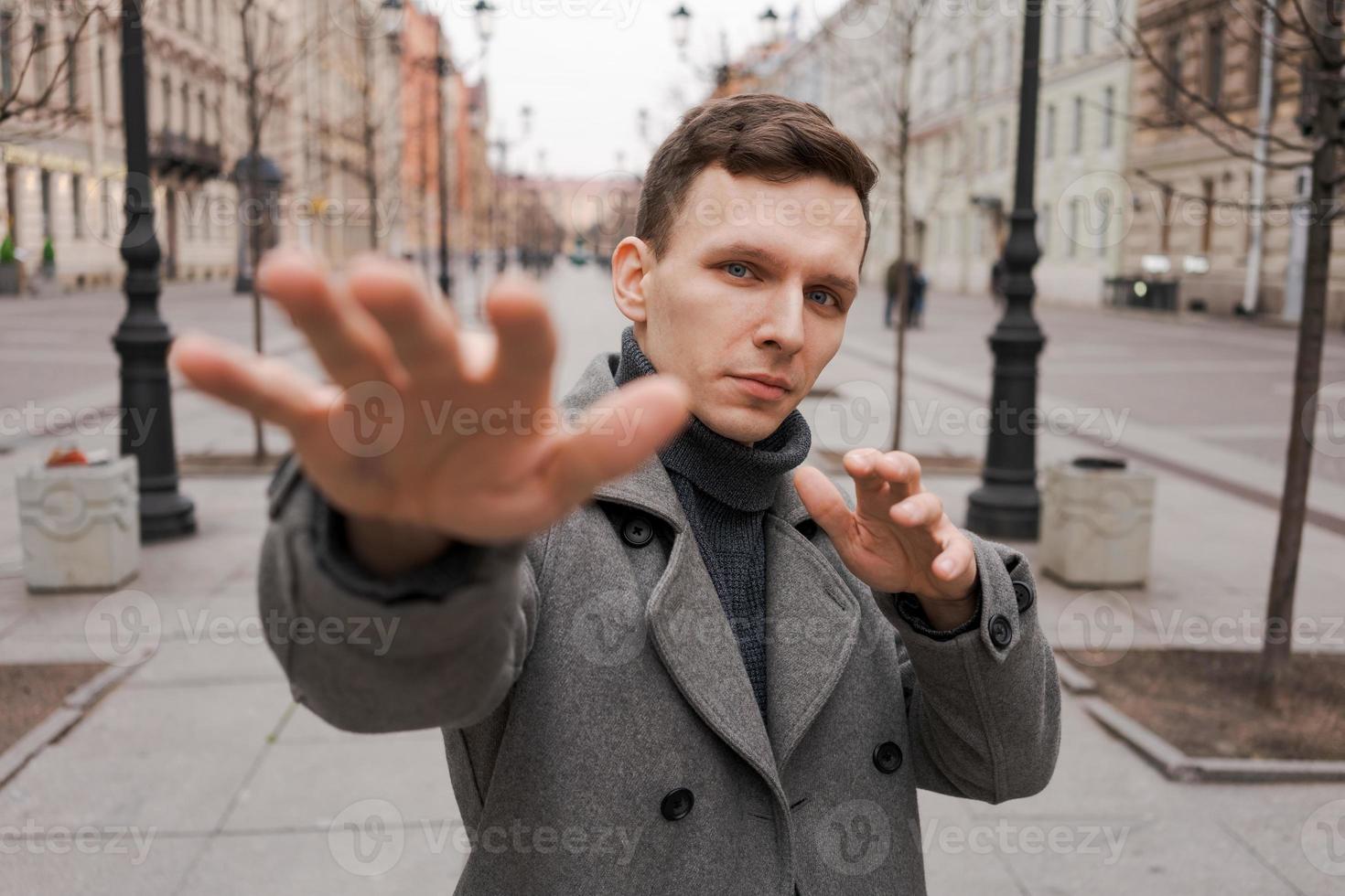 Young man in dark clothes on street. Caucasian guy in gray coat, smiles photo