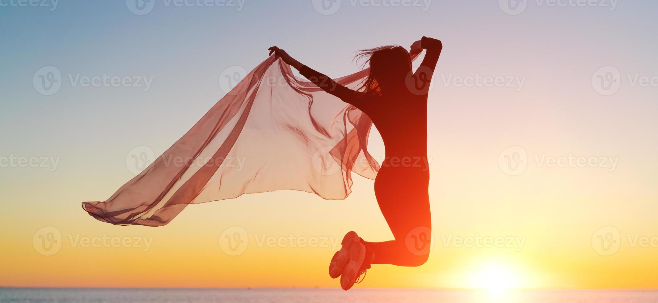 Silhouette slender girl at sunset on seashore rejoices with a transparent cloth photo