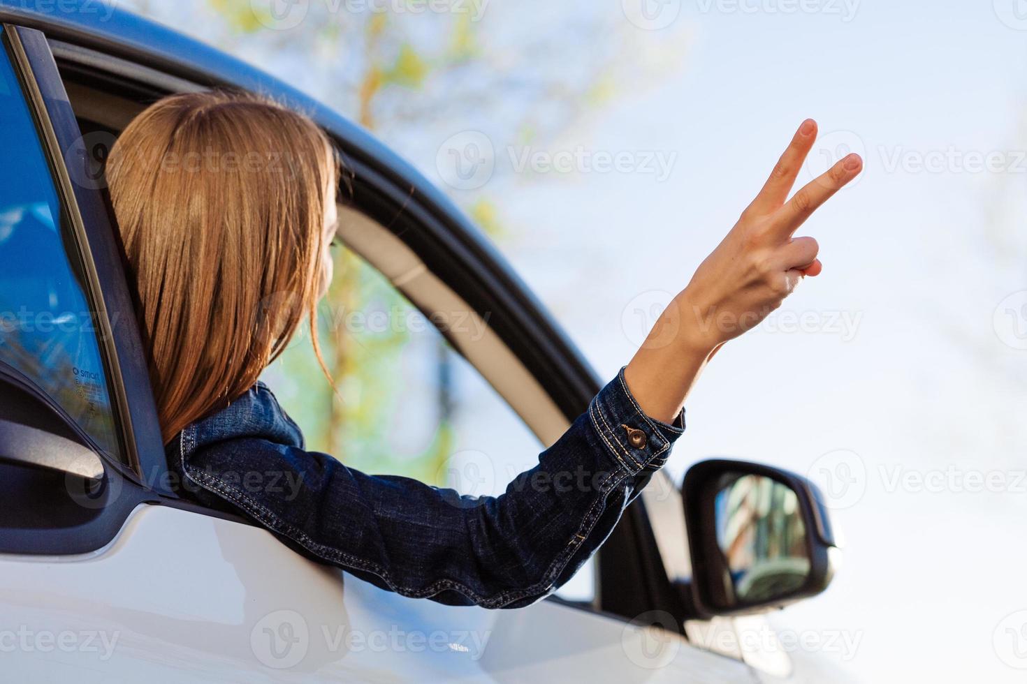 Happy woman waving her hand on an open windowed car against blue sky and sun. photo