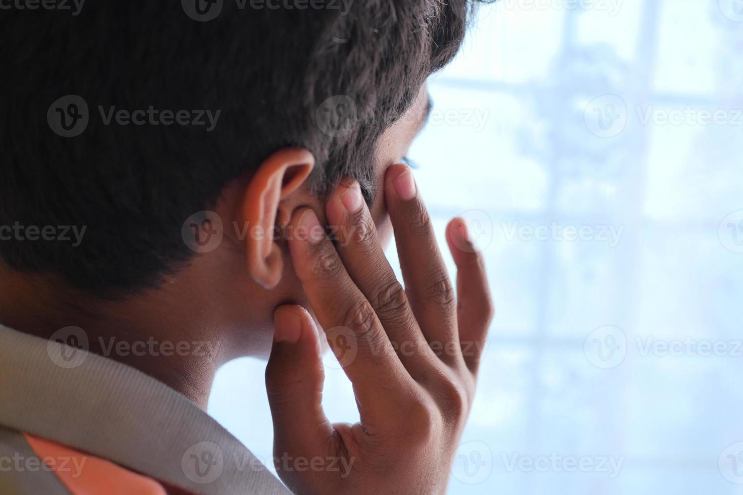 teenage boy having ear pain touching his painful ear , photo