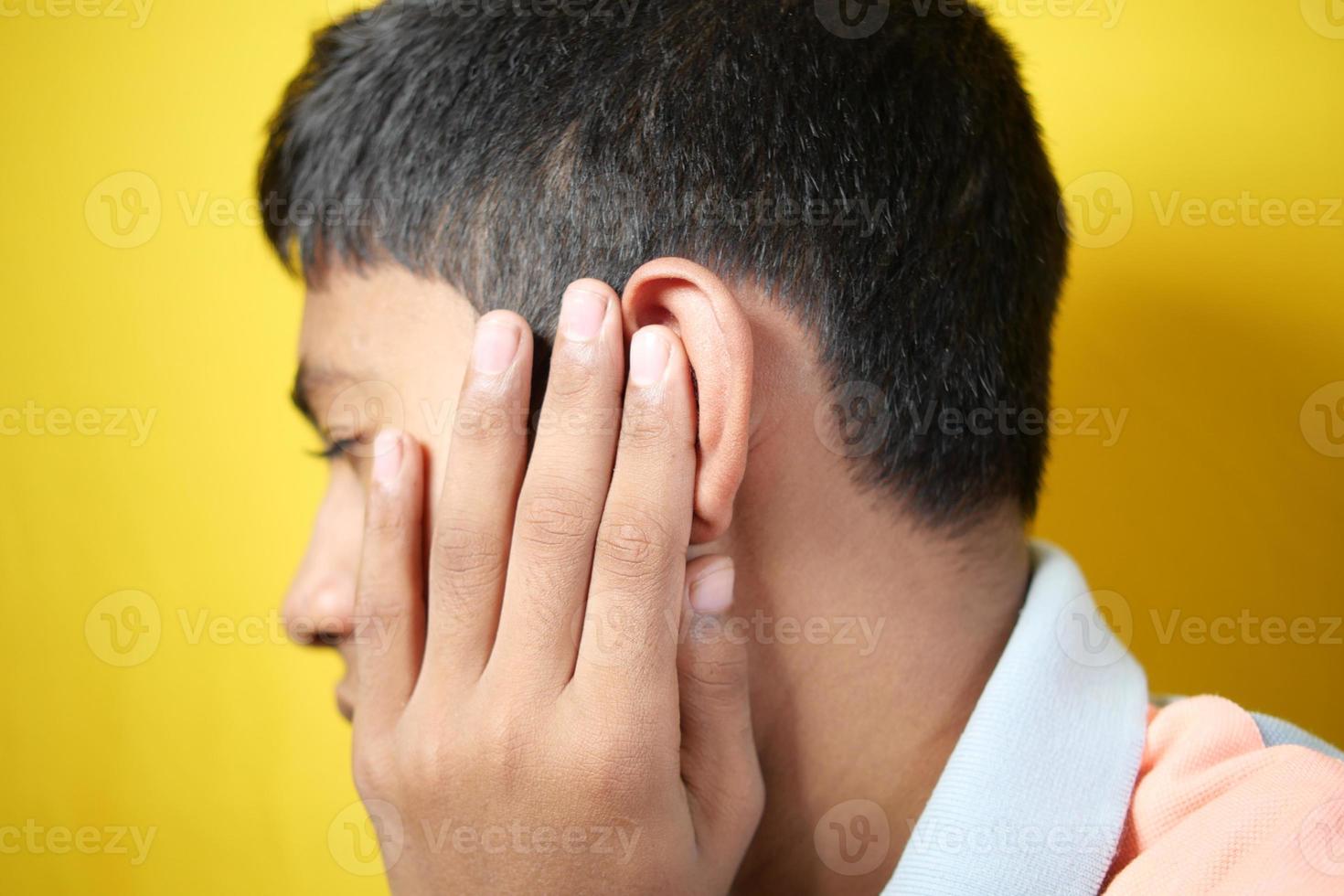 teenage boy having ear pain touching his painful ear , photo