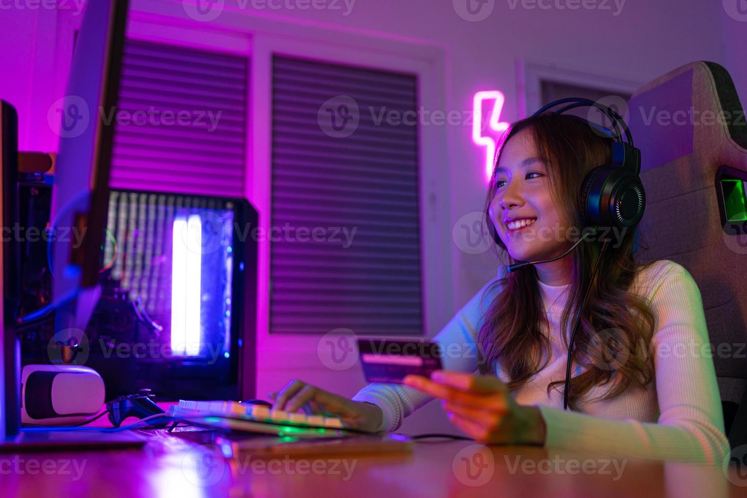 Top up online game with credit card concept. Gamer and E-Sport online of Asian woman playing online computer video game with lighting effect, broadcast streaming live at home. Gamer and E-Sport gaming photo
