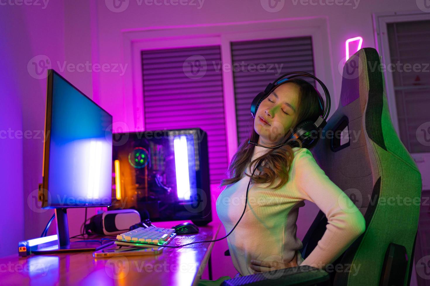 Young people Backache. Gamer and E-Sport online of Asian woman playing online computer video game with lighting effect, broadcast streaming live at home. She a backache due to sitting for a long time photo