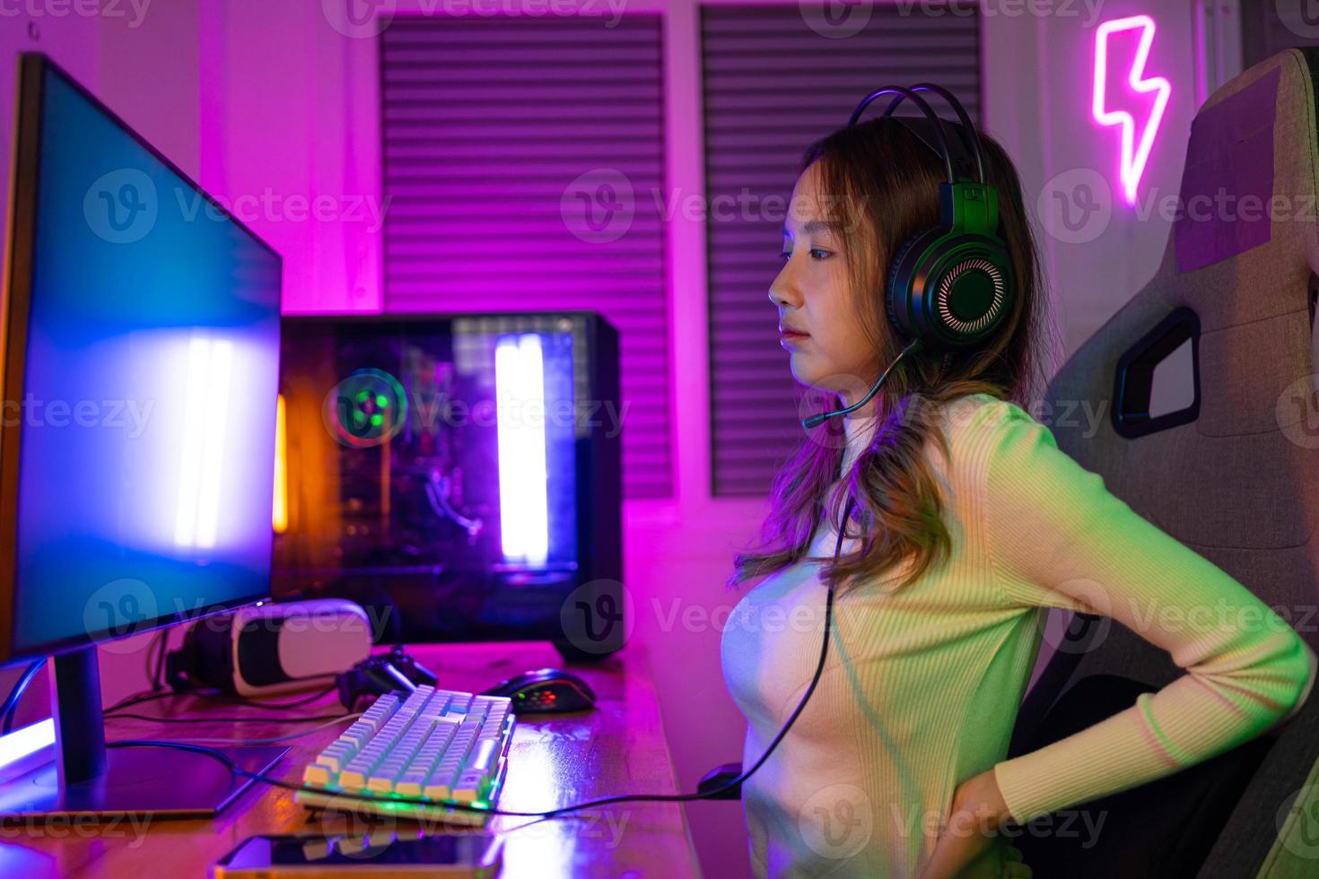 Young people Backache. Gamer and E-Sport online of Asian woman playing online computer video game with lighting effect, broadcast streaming live at home. She a backache due to sitting for a long time photo