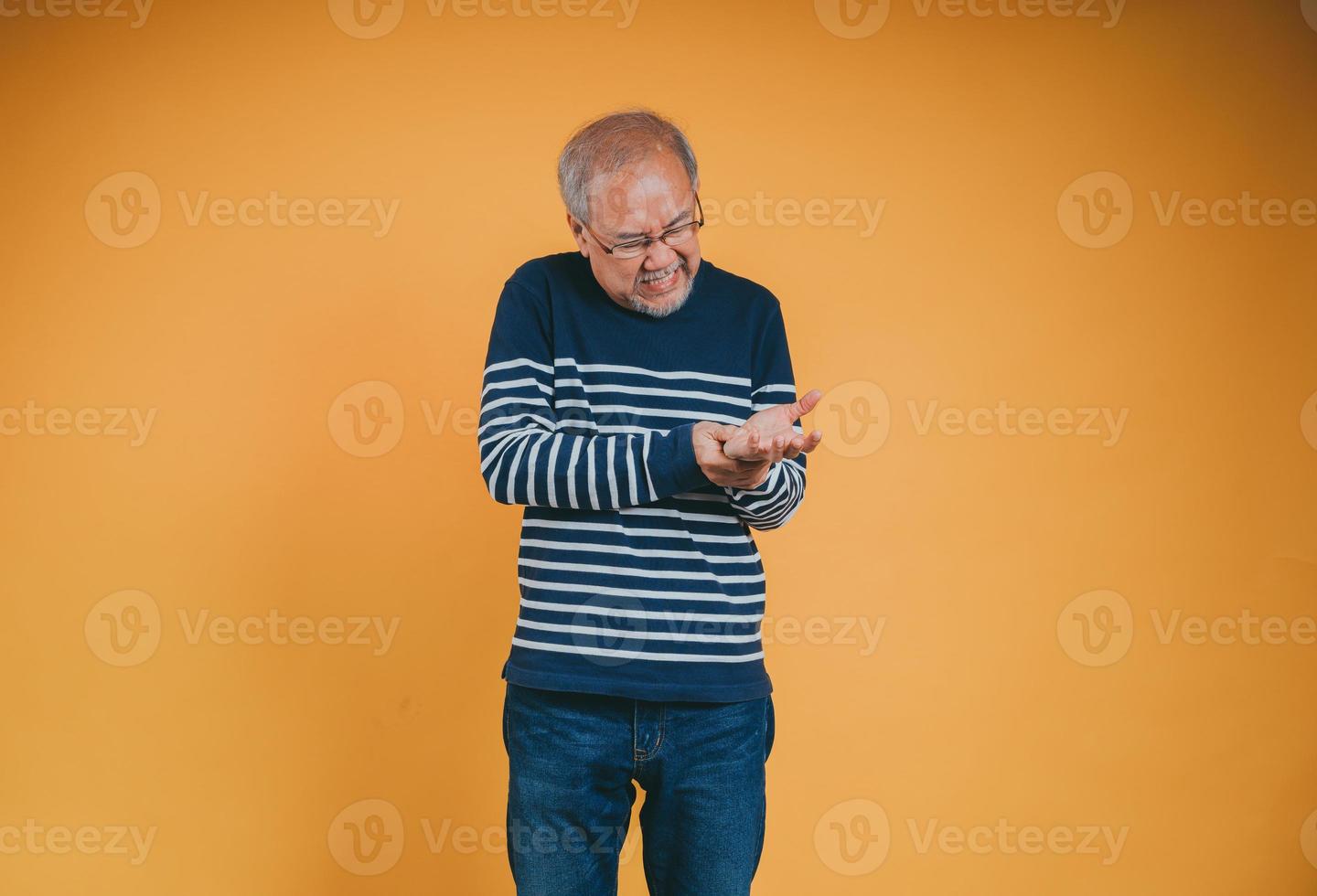 Asian senior man feeling wrist pain on the yellow background. photo