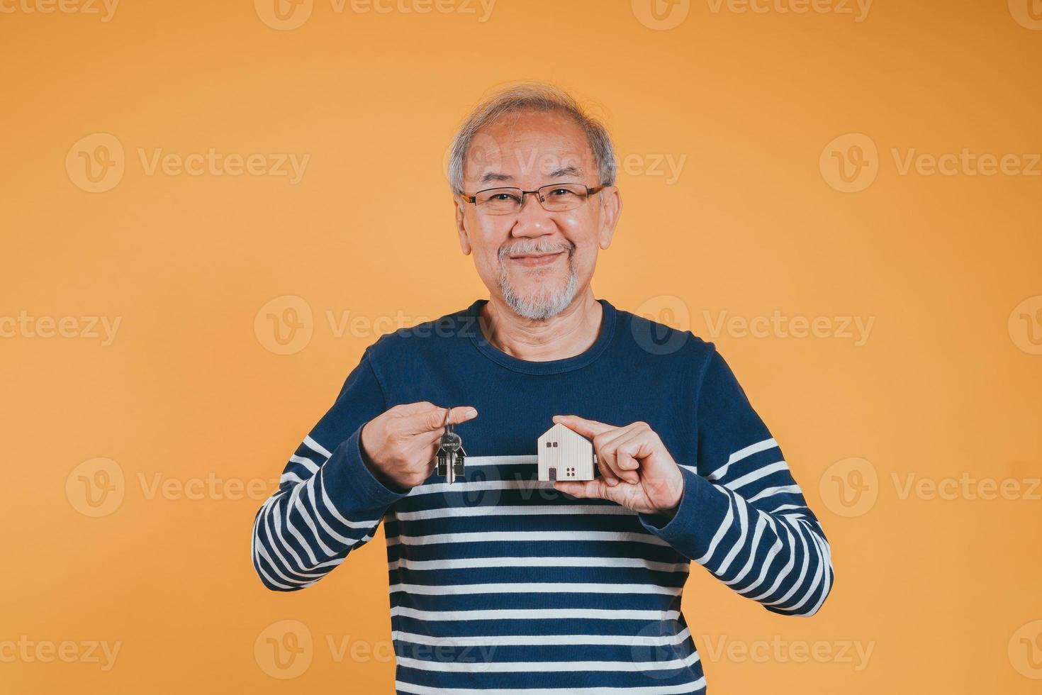Senior male holding wooden house model property owner after retirement on yellow background. photo