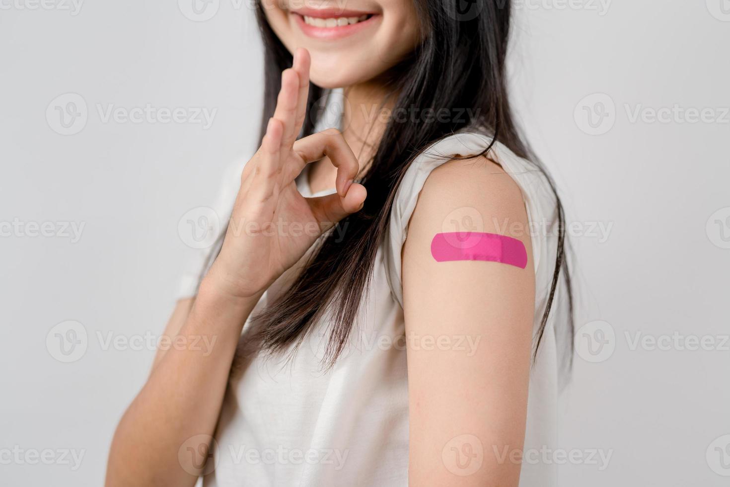 contento joven mujer espectáculo Okay firmar después consiguiendo un vacuna. demostración hombro con vendaje después recepción vacunación, manada inmunidad, lado efecto, aumentador de presión dosis, vacuna pasaporte y coronavirus pandemia foto