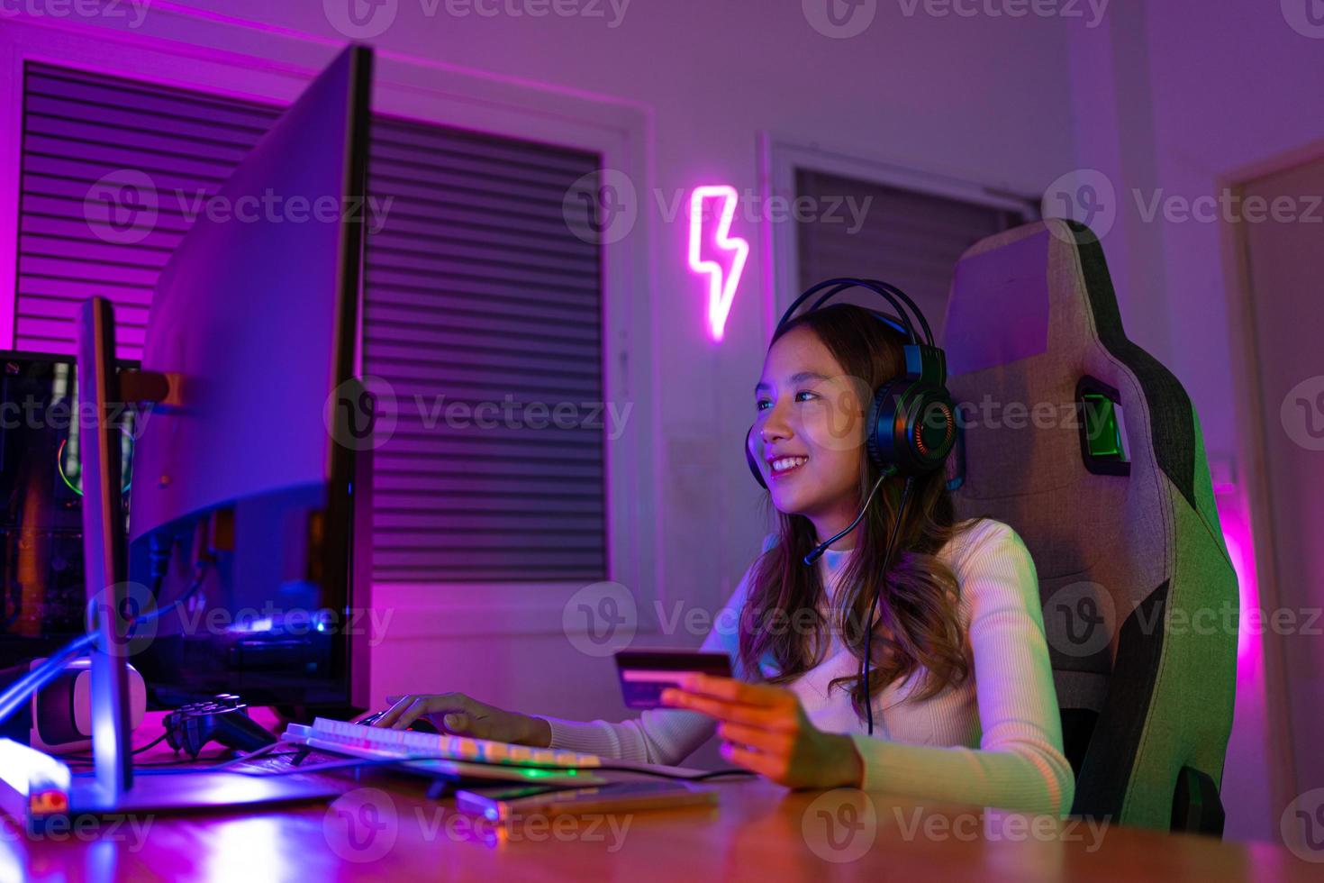 Top up online game with credit card concept. Gamer and E-Sport online of Asian woman playing online computer video game with lighting effect, broadcast streaming live at home. Gamer and E-Sport gaming photo