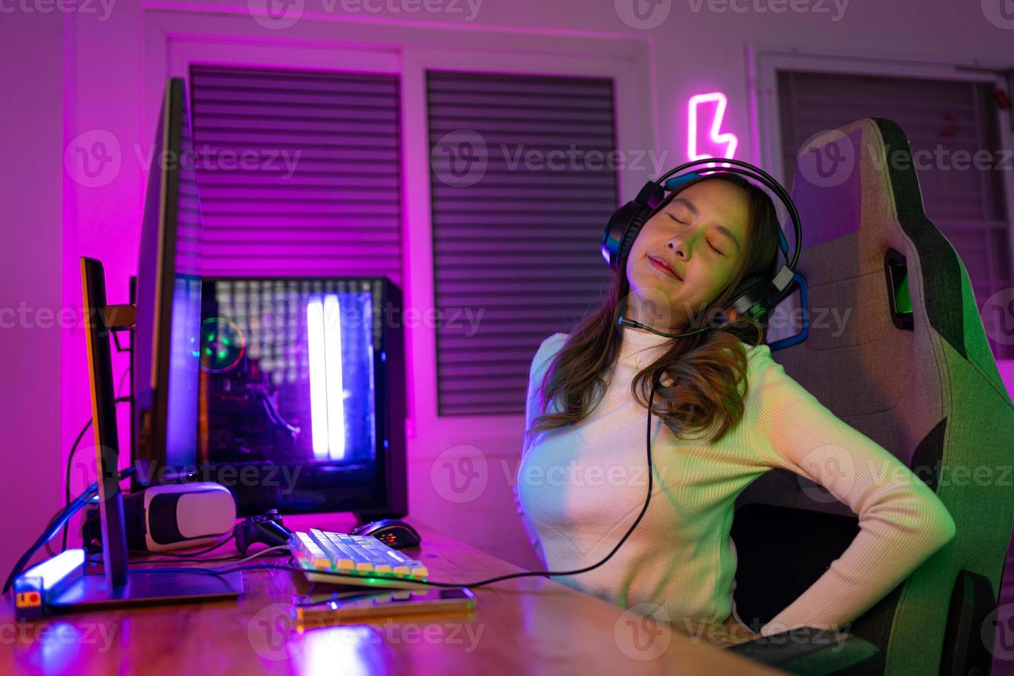 Young people Backache. Gamer and E-Sport online of Asian woman playing online computer video game with lighting effect, broadcast streaming live at home. She a backache due to sitting for a long time photo