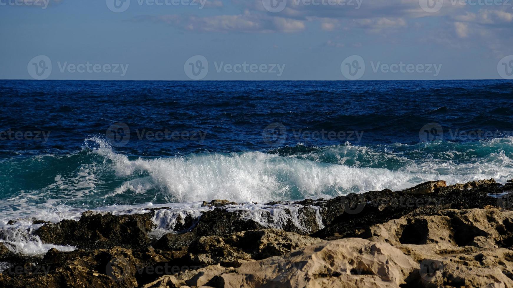Blue sea wave and white foam and splash. Stone beach on island of Malta, no sandy beach. Summer holiday border frame concept. Tropical island vacation backdrop. Tourist travel banner design template. photo