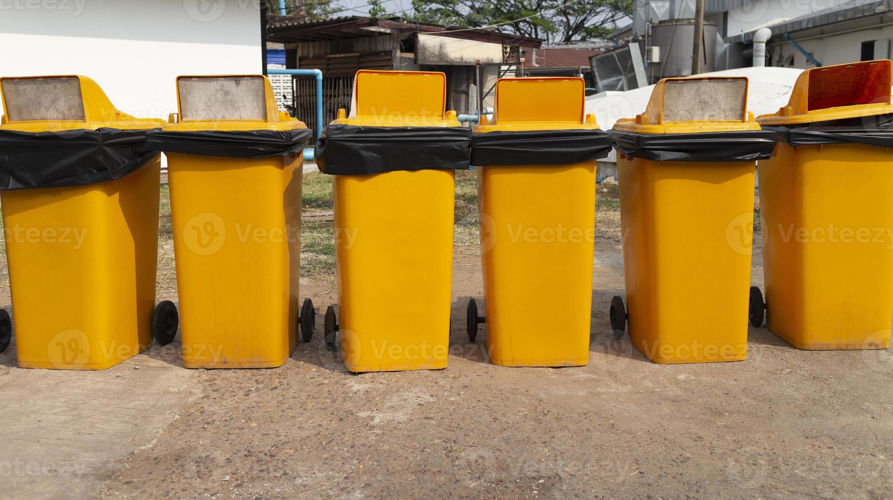 Several yellow plastic bins arranged outside a building by six identical yellow bins. photo