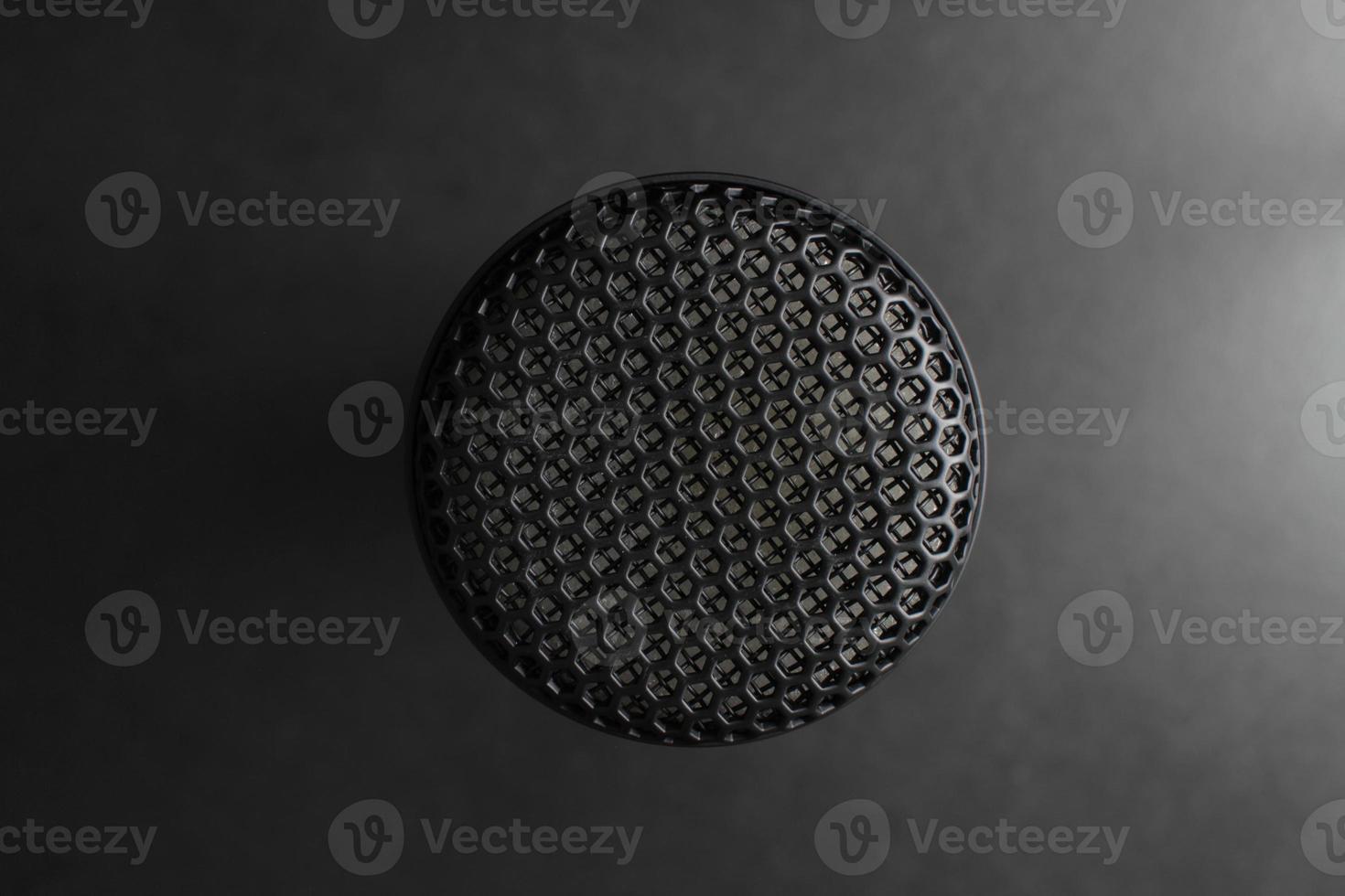 Close-up shot, the top of the microphone against a black background with studio lighting in the same tone. photo