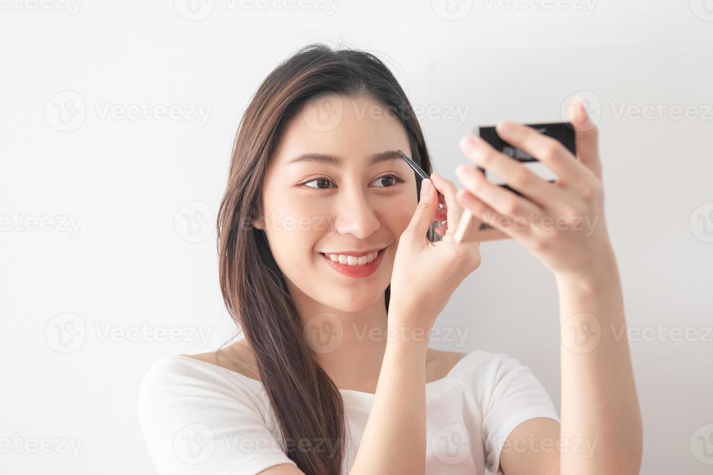 Eyeshadow applying concept, portrait of beauty young asian woman make up for eyes, eyebrow close up. Female look face with natural fashion style, holding the mirror, isolated on white background. photo