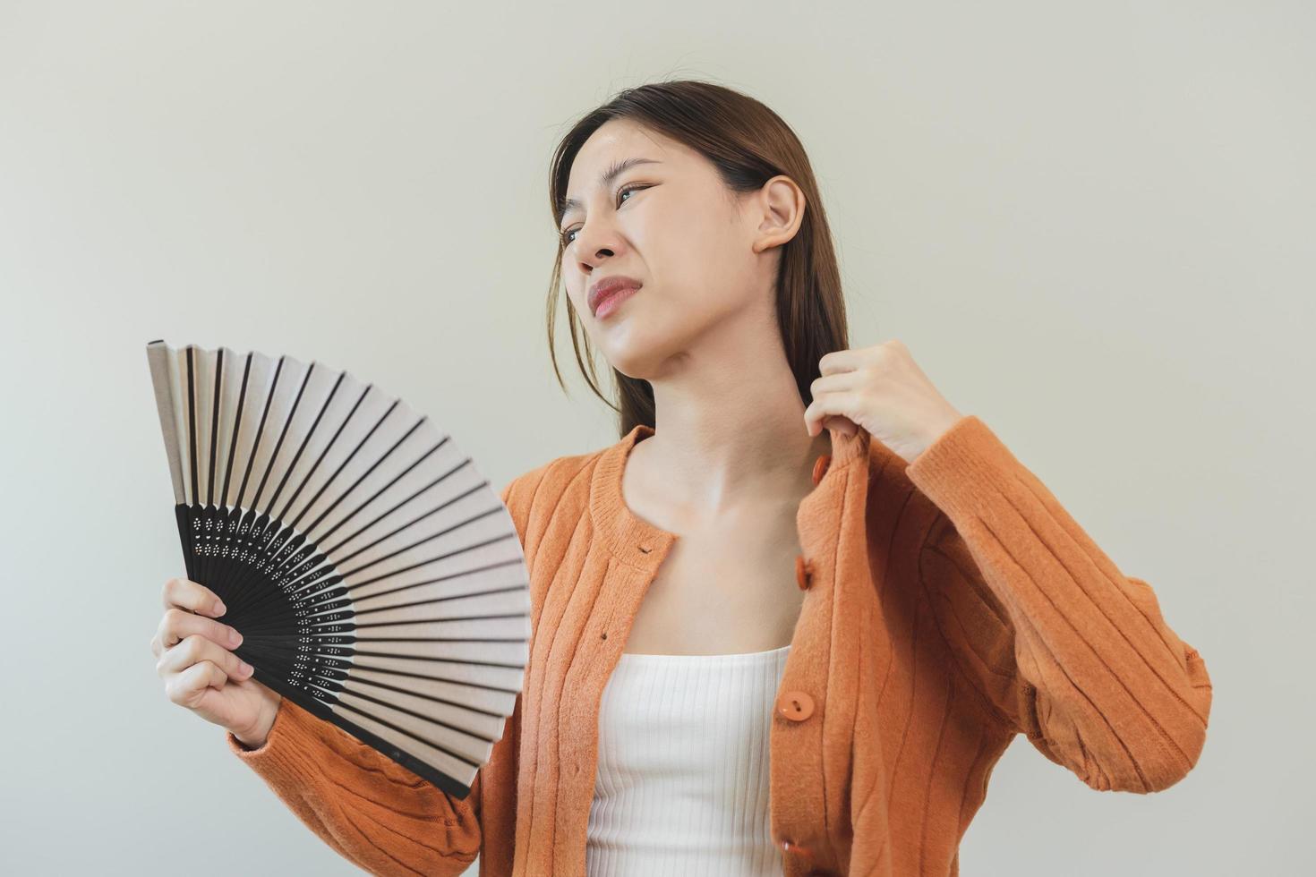 Suffering summer heat stroke, hot weather, tired asian young woman, girl sweaty and thirsty, refreshing with hand in blowing, wave fan to ventilation when temperature high at home, house on background photo