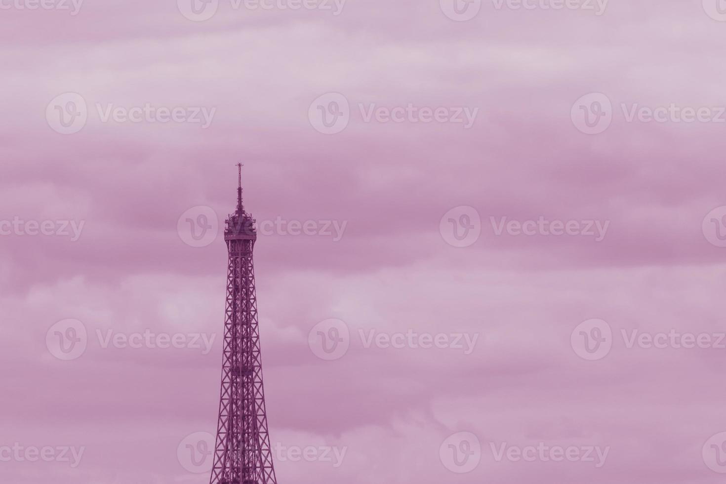 top part of Eiffel Tower in Paris against clouds colored in pink photo