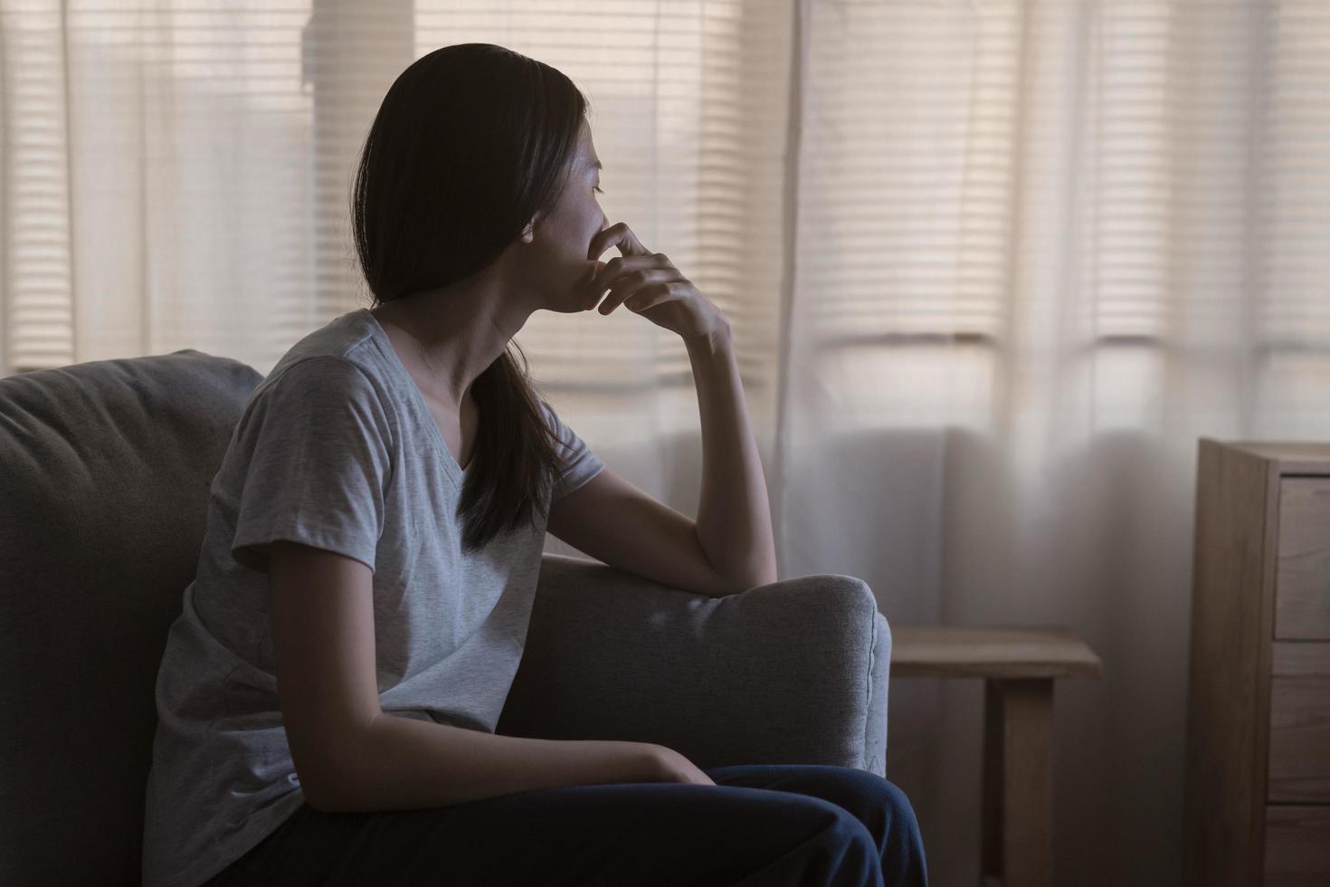 Mental health, depressed sad asian young woman, girl sitting on sofa, couch, expression to face difficulty, failure and exhausted. Thoughtful worried suffering depression feeling lonely, alone at home photo