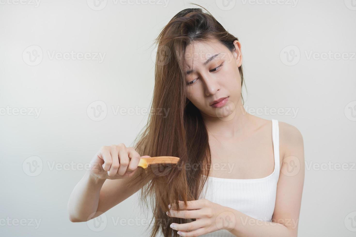 Damaged Hair, frustrated asian young woman, girl hand in holding brush splitting ends messy while combing hair, unbrushed dry long hair. Health care beauty, portrait isolated on white background. photo