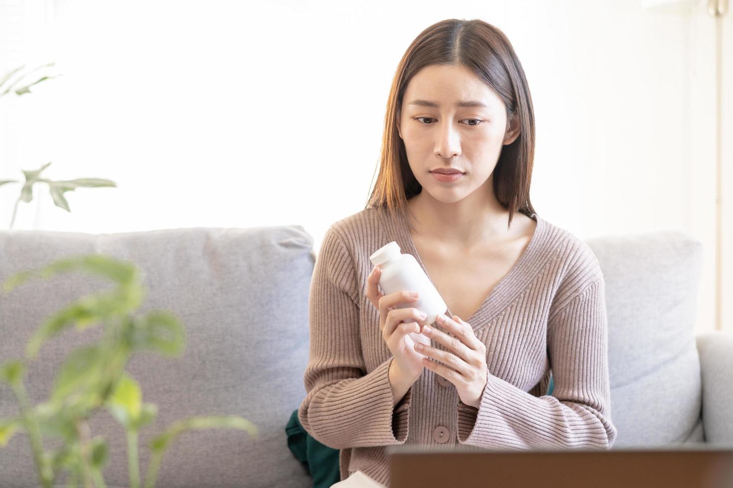 enfermedad asiático joven mujer participación medicina botella, consultante salud por telesalud en línea con médico acerca de síntoma estómago dolor, utilizar ordenador portátil computadora. telemedicina por médico para distancia paciente. foto