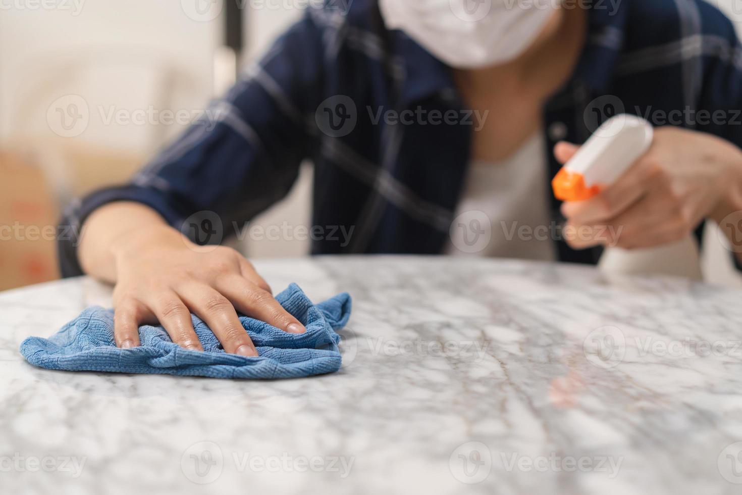 limpieza higiene, cerca arriba mano de joven mucama mujer vistiendo protector guantes mientras limpieza en blanco mármol mesa, utilizar azul trapo limpiando a polvo y rociar en restaurante. limpieza interna limpiar, limpiador. foto