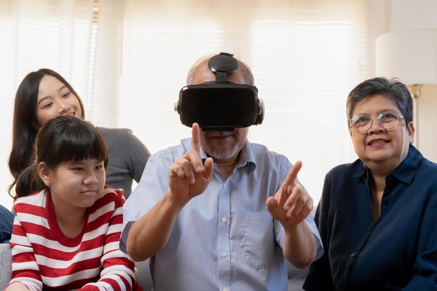 contento familia asiático Envejecido abuelo, abuela tener divertido, sonriente padre y hermanas, hombre vistiendo virtual realidad anteojos, utilizando con vr gafas de protección auriculares disfrutar fin de semana juntos en vivo habitación a hogar. foto