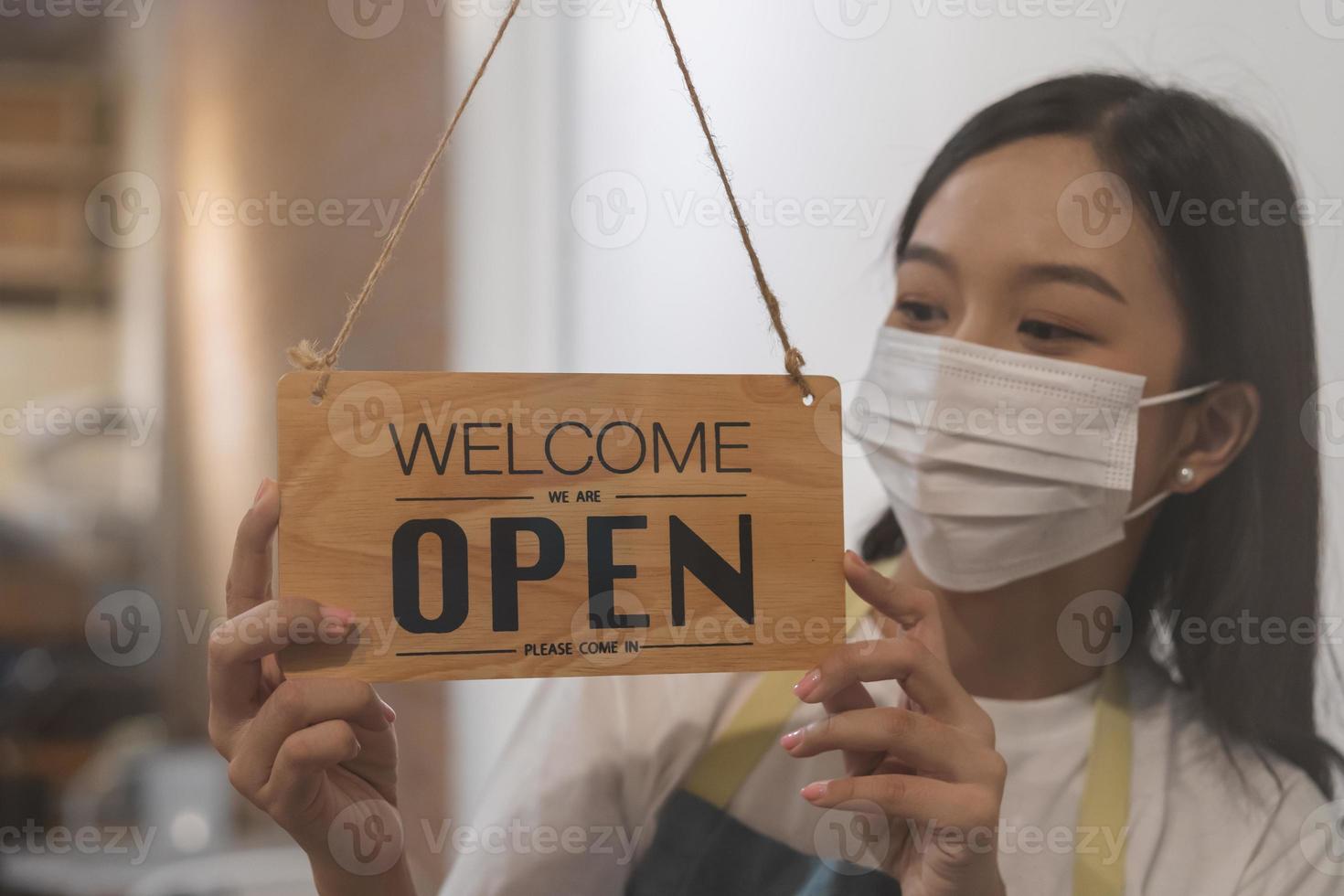 reabrir, asiático joven propietario minorista, café tienda mujer torneado firmar tablero abierto vistiendo cara mascarilla, proteger a pandemia de coronavirus, reabrir Tienda después cerca encierro cuarentena en COVID-19, nuevo normal. foto