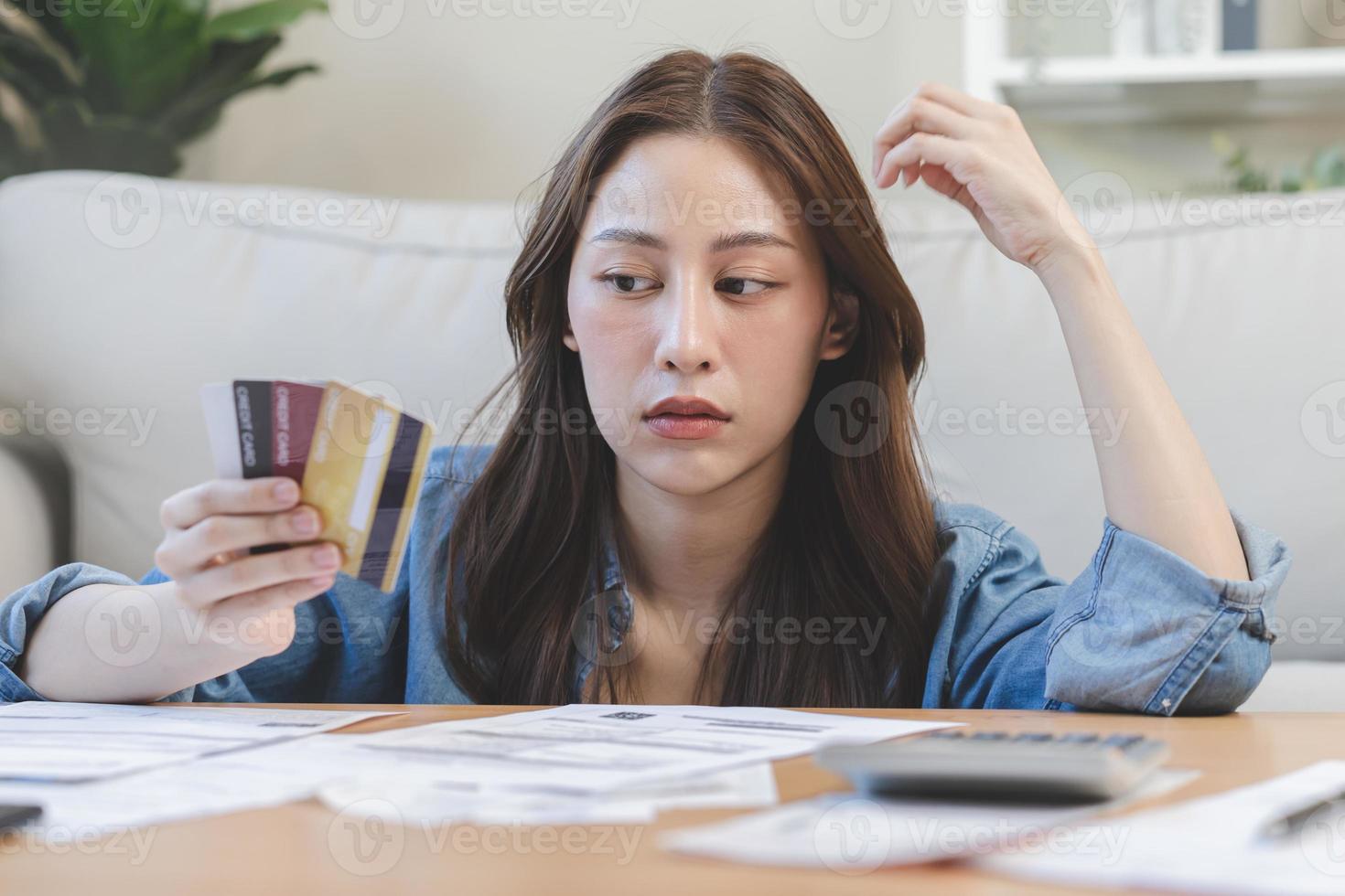 Financial owe asian woman, female hand in cover face, sitting in stressed and confused by calculate expense from invoice or bill, have no money to pay, mortgage or loan. Debt, bankruptcy or bankrupt. photo