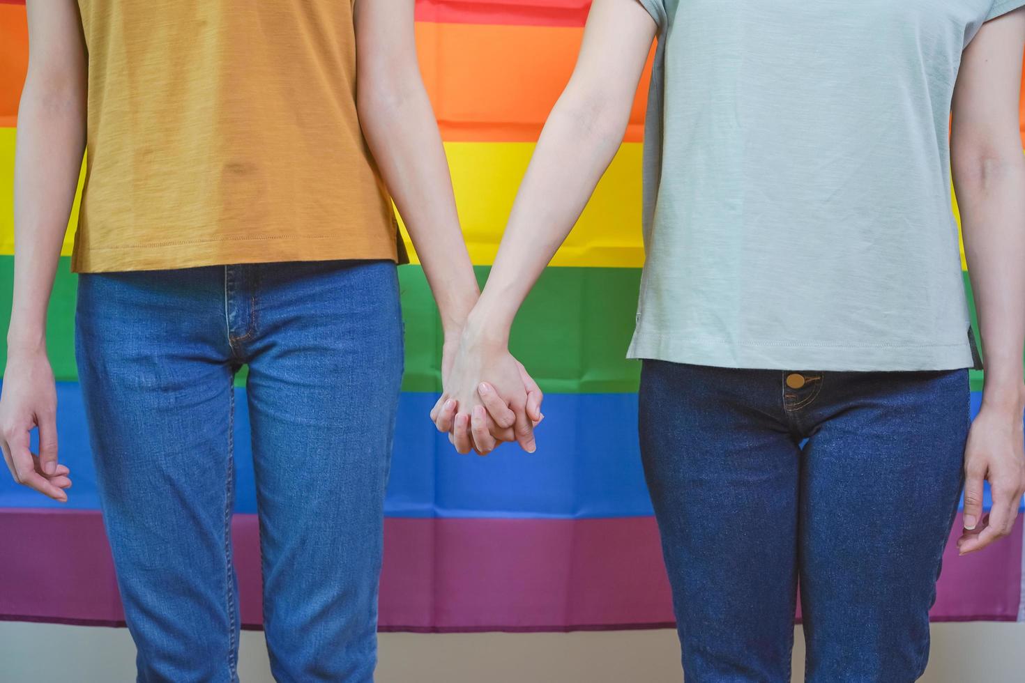 Happy lesbian, beautiful asian young two women, girl gay or lgbt, lgbtq couple love moment spending good time, stand together holding hands in front of pride rainbow flag symbol on isolated background photo