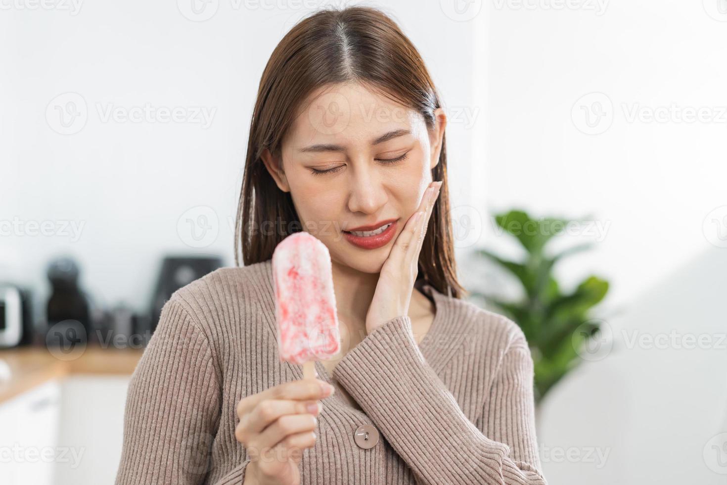 salud asiático joven mujer conmovedor mejilla, expresión, sufrimiento desde dolor de muelas, decaer o sensibilidad cavidad molar diente, dientes o inflamación comer frío hielo crema a hogar. sensible dientes gente. foto