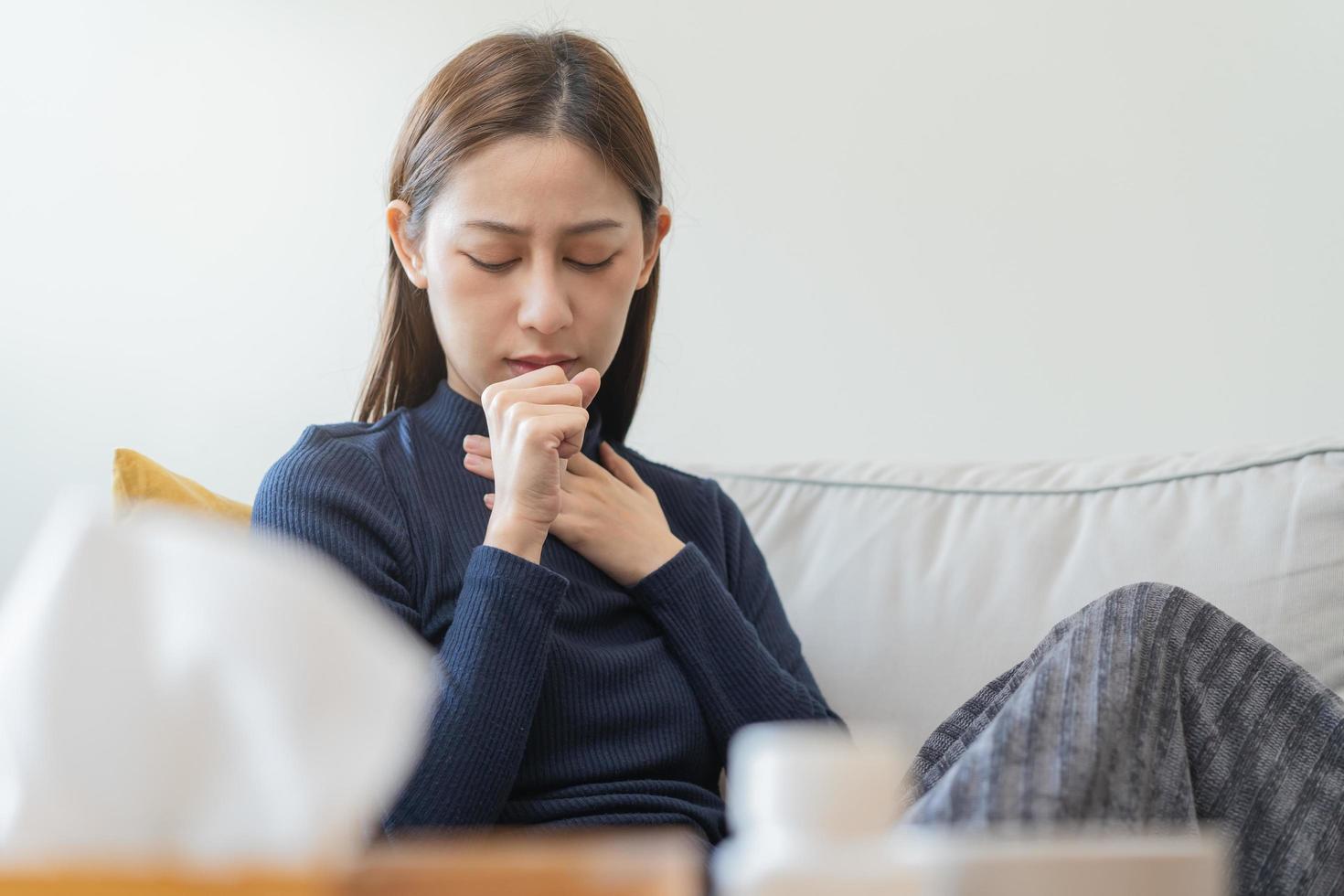 Sick, hurt or pain asian young woman, girl with sore throat, cough have a fever, flu and sneezing nose, runny sitting on sofa bed at home. Health care person on virus seasonal. photo