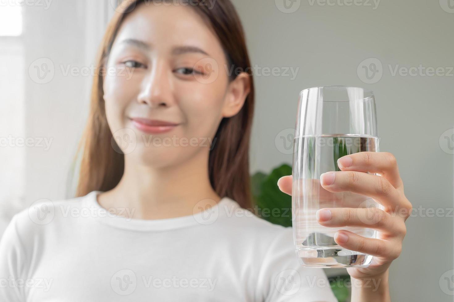 contento hermoso, asiático joven mujer, niña Bebiendo, sorbo Fresco vaso de agua para hidratación de cuerpo, participación transparente vaso en su mano, sediento a hogar. salud cuidado, sano estilo de vida concepto. foto