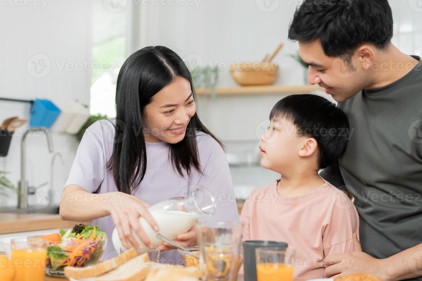 contento refresco familia desayuno en mañana, asiático joven padre padre, madre y pequeño linda chico, niño teniendo comida en cocina comiendo juntos a hogar. alegre, disfrutar Cocinando gente. foto