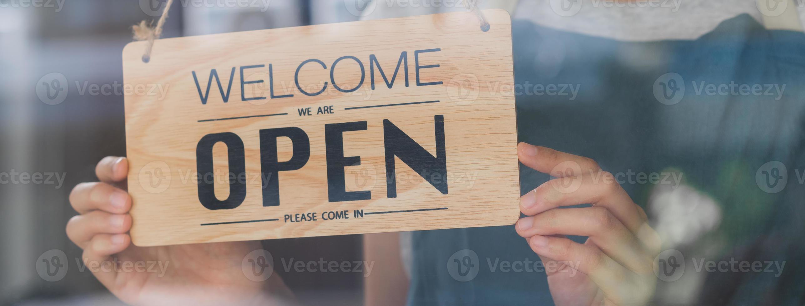 Owner business retail, asian young woman hand in turning sign board to open coffee shop, wearing face mask protect to pandemic of coronavirus, reopen store after close lockdown quarantine in covid-19. photo